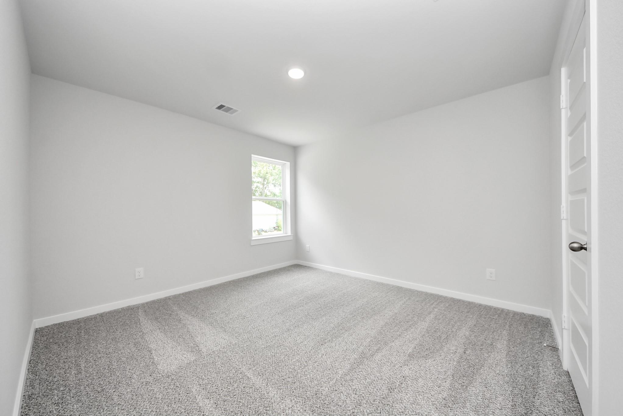 Bright, carpeted bedroom with neutral walls in The Sabine E floor plan at Windmill Estates, Magnolia, Texas.