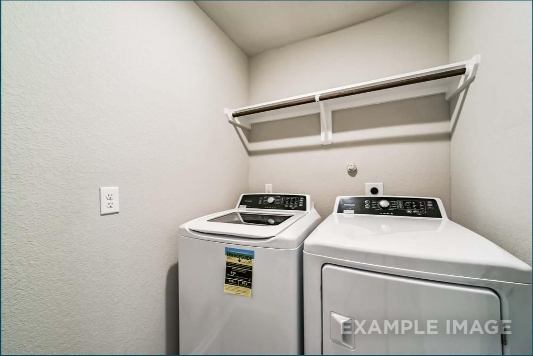 Modern laundry room with white front-load washer and dryer, overhead shelves in Davidson Homes Riviera C, Dayton Texas