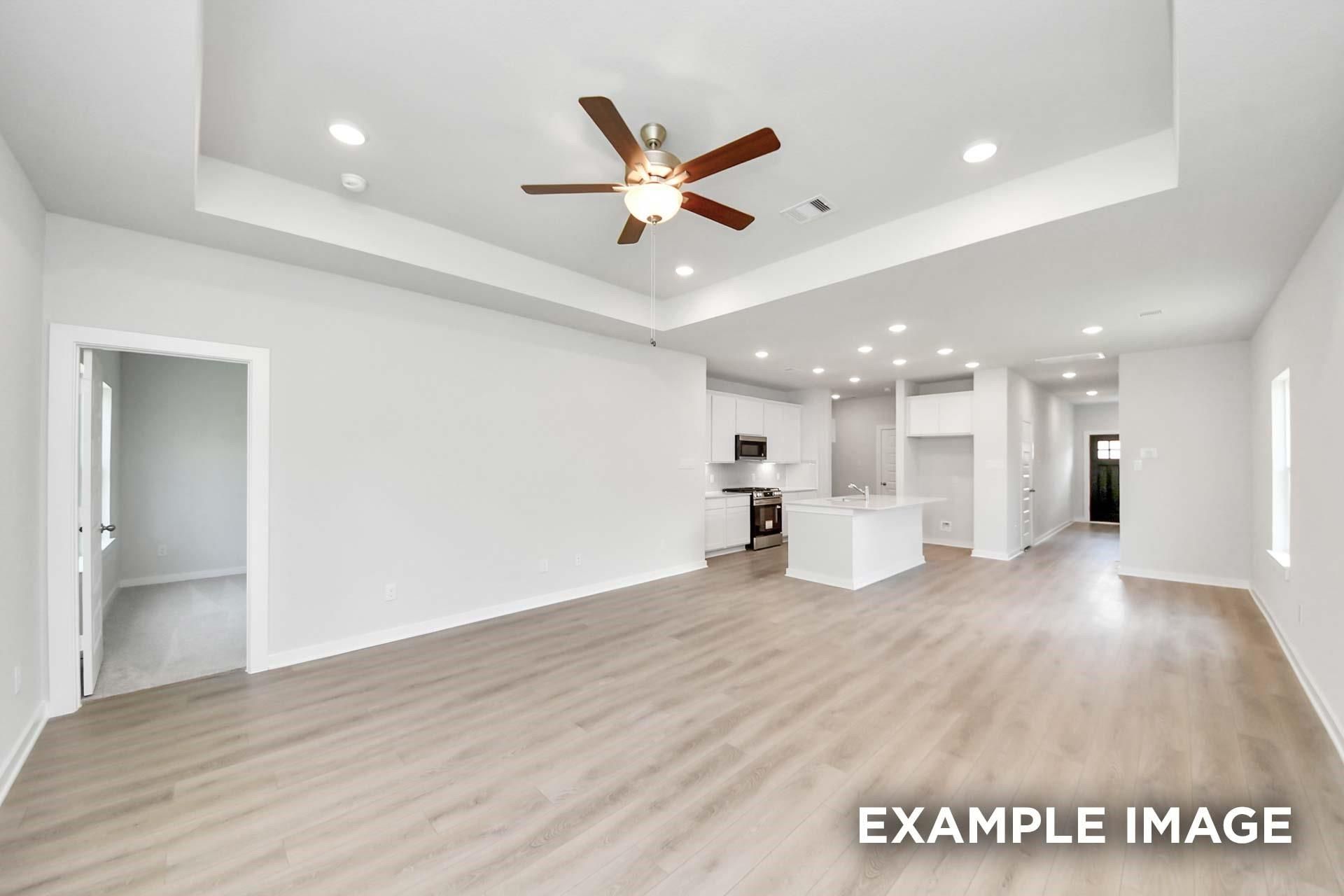 Open-concept living area with tray ceiling and LVP flooring flowing to white kitchen in Davidson Homes The Blanco E, Magnolia