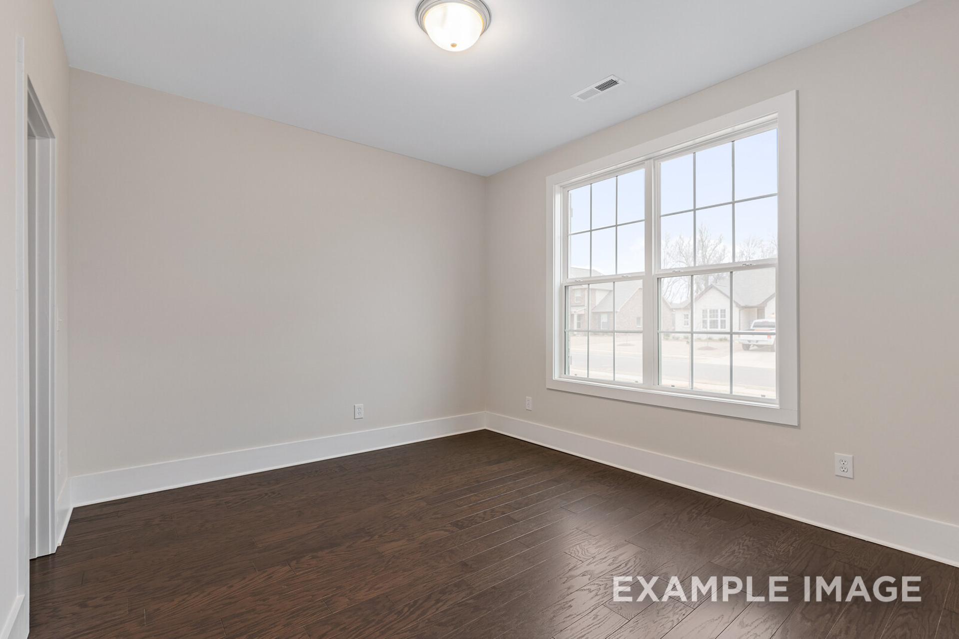 Spacious bedroom in The Rockford by Davidson Homes with beige walls, dark hardwood floors, and large sunny window
