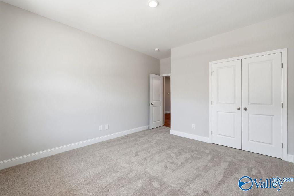 Spacious bedroom featuring gray carpet, light gray walls, double closet doors, and adjacent bath entry in Davidson Homes The Harrison, Hartselle AL