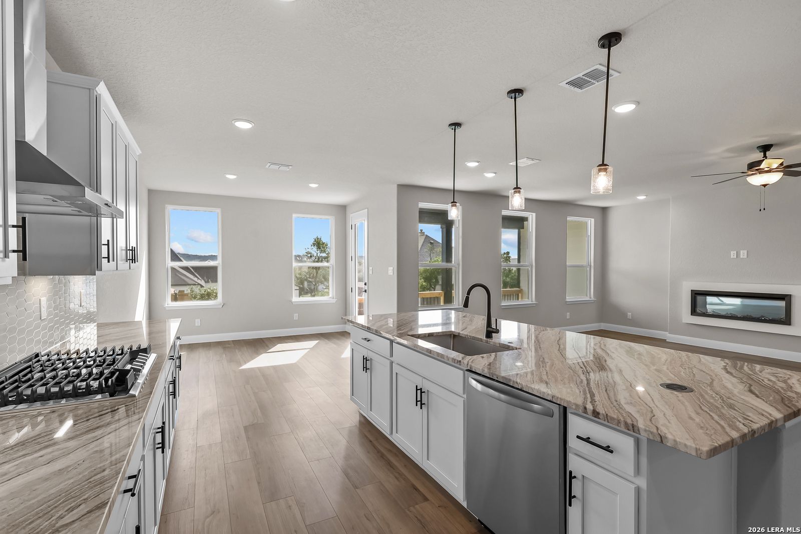 Open-concept kitchen with marble island, gray cabinets, and hardwood floors in Davidson Homes Foster E plan, Castroville, TX