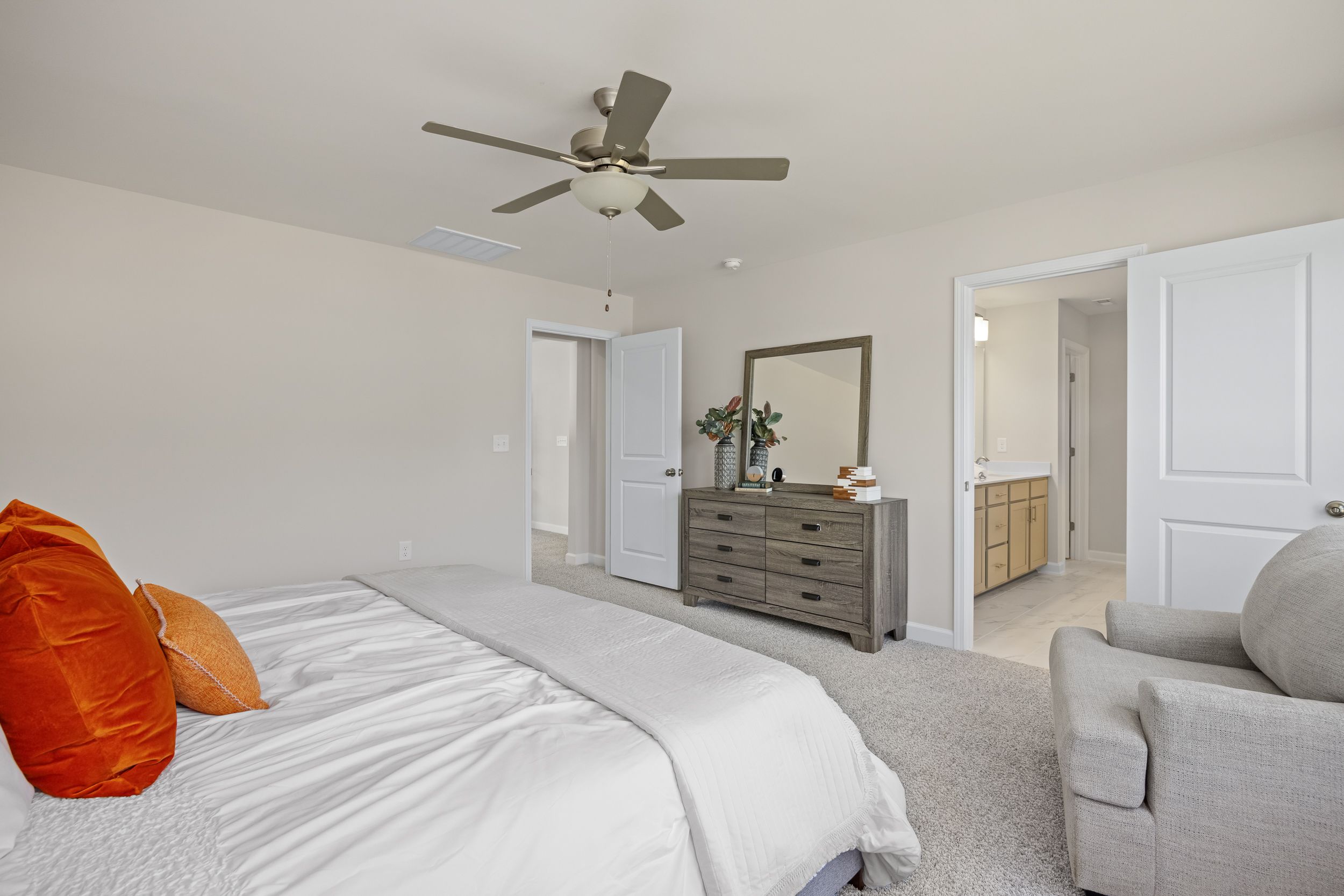 Master bedroom at Montrose in Aberdeen NC with king bed orange accent pillows wooden dresser ceiling fan and en-suite bath by Davidson Homes