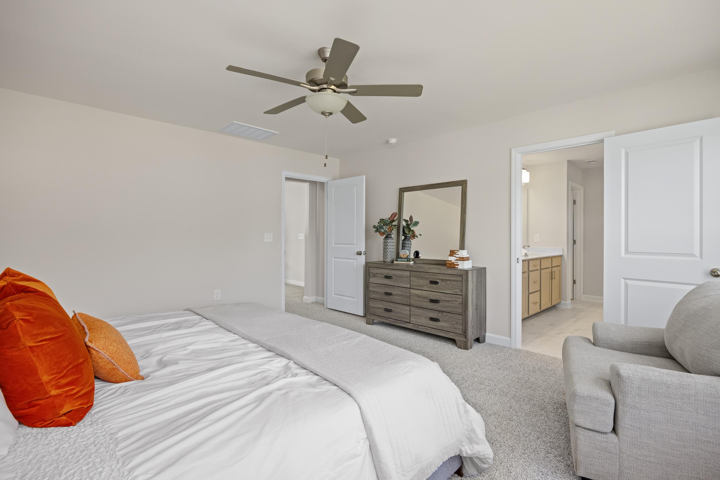 Master bedroom at Montrose in Aberdeen NC with king bed orange accent pillows wooden dresser ceiling fan and en-suite bath by Davidson Homes