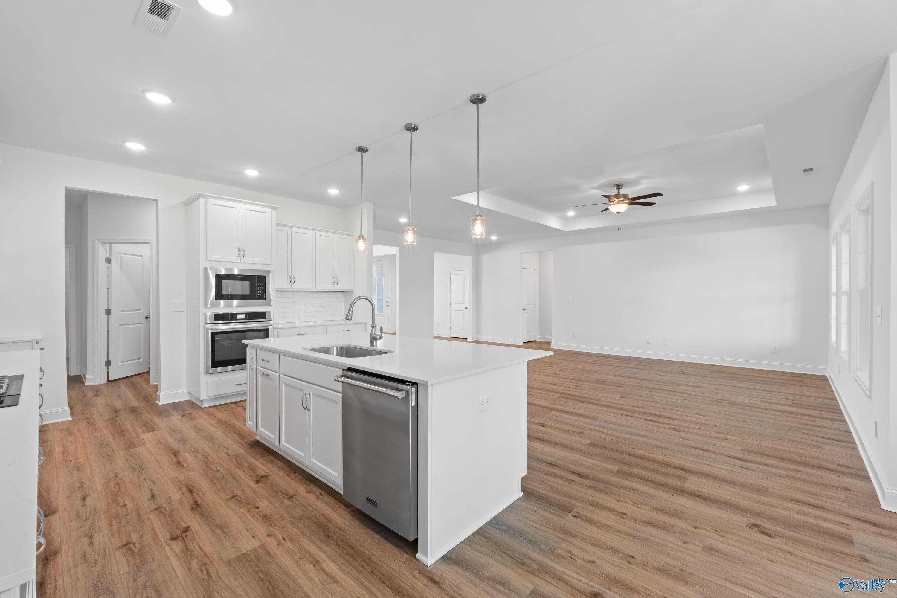 Modern white open-concept kitchen with large island, stainless dishwasher, double ovens, and adjacent living area in The Oxford floor plan, Harvest, AL