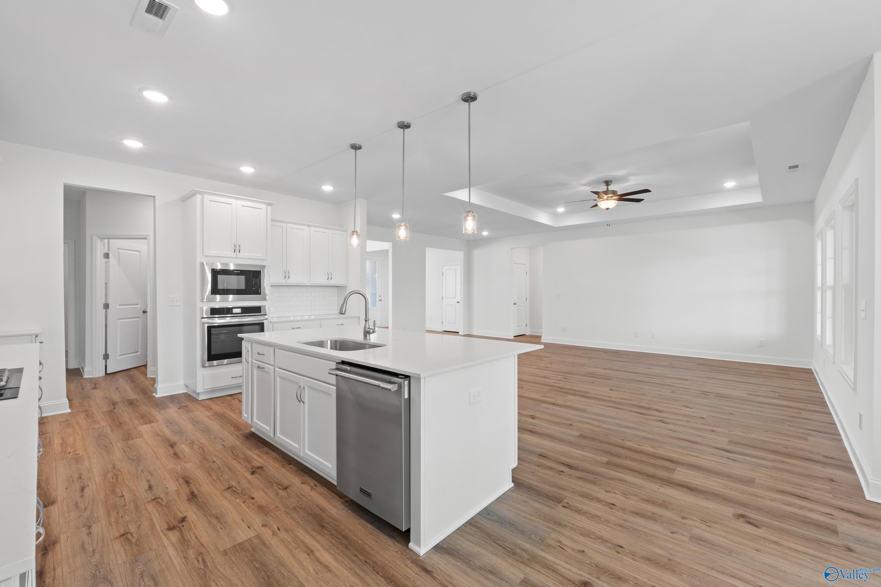 Modern white open-concept kitchen with large island, stainless dishwasher, double ovens, and adjacent living area in The Oxford floor plan, Harvest, AL
