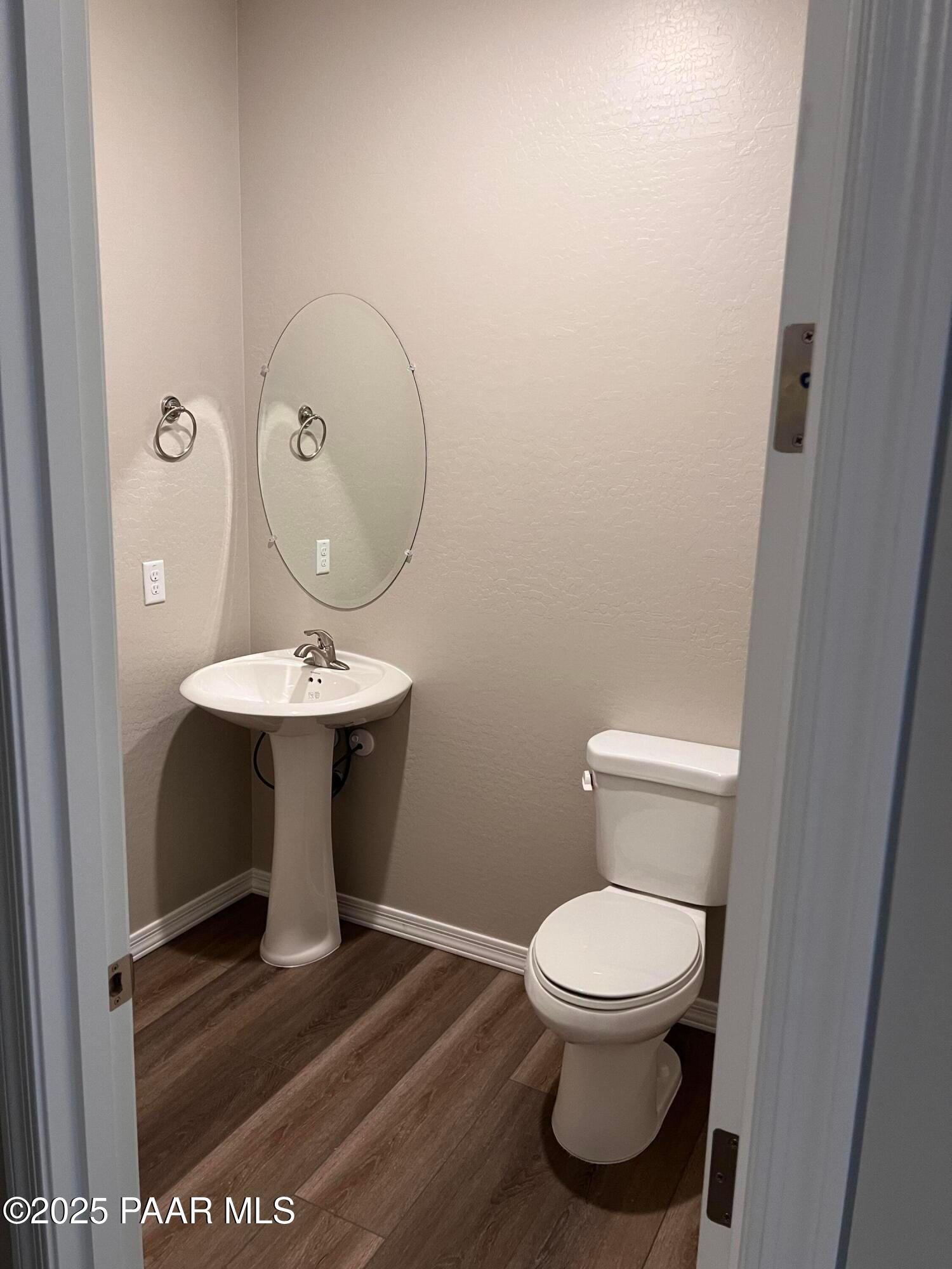 Elegant powder room with pedestal sink, round mirror, and luxury vinyl plank flooring in Davidson Homes The Harmony A, Prescott Valley, AZ