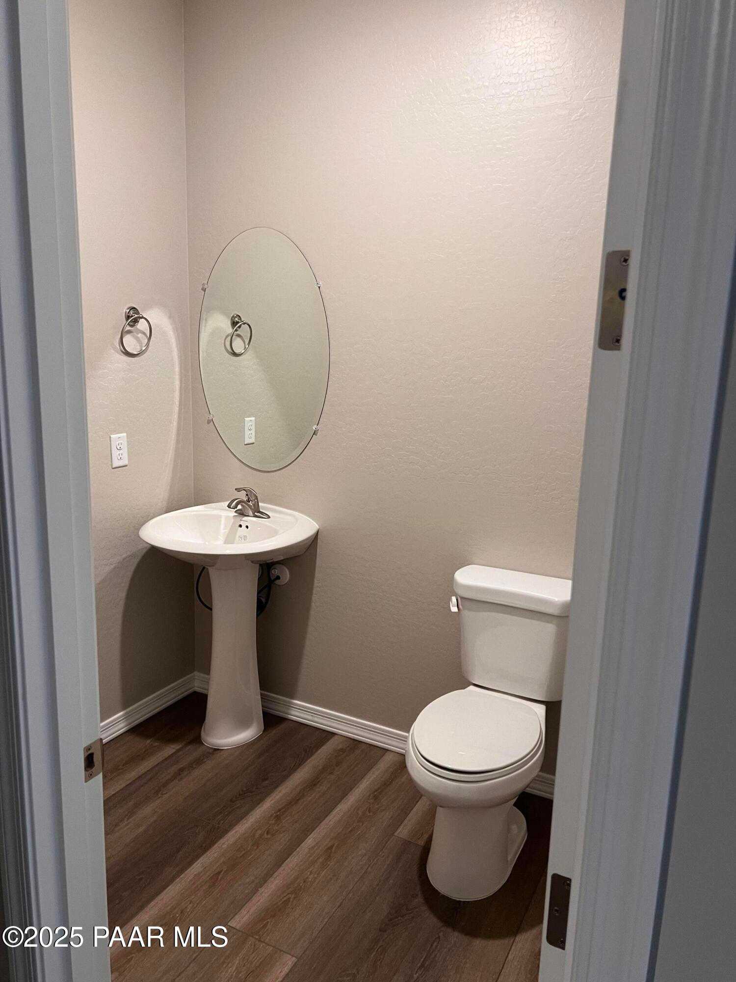 Elegant powder room with pedestal sink, round mirror, and luxury vinyl plank flooring in Davidson Homes The Harmony A, Prescott Valley, AZ