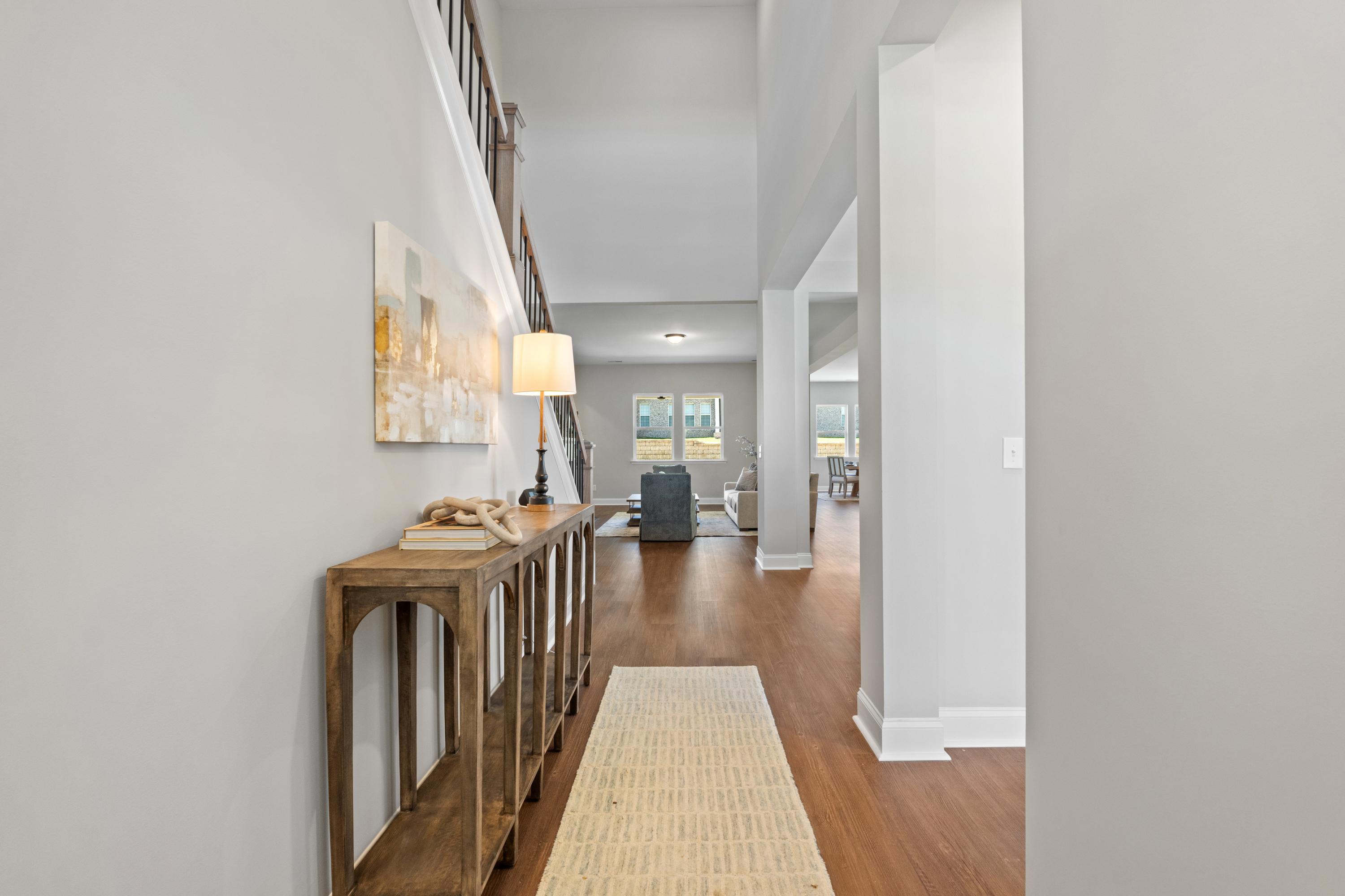 Spacious entryway in The Haven D showcasing wooden console table, lamp, abstract art, and open living area with hardwood floors