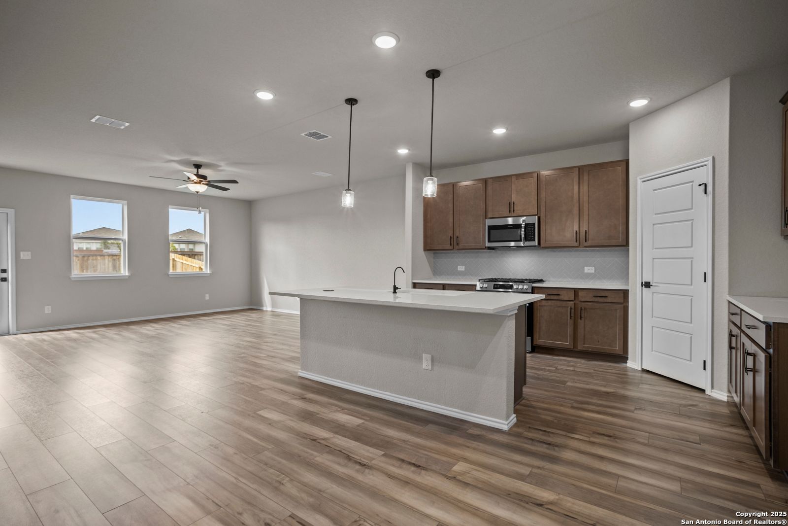 Spacious open kitchen with large white island, brown cabinets, stainless appliances, and hardwood floors in Davidson Homes The Douglas F, San Antonio