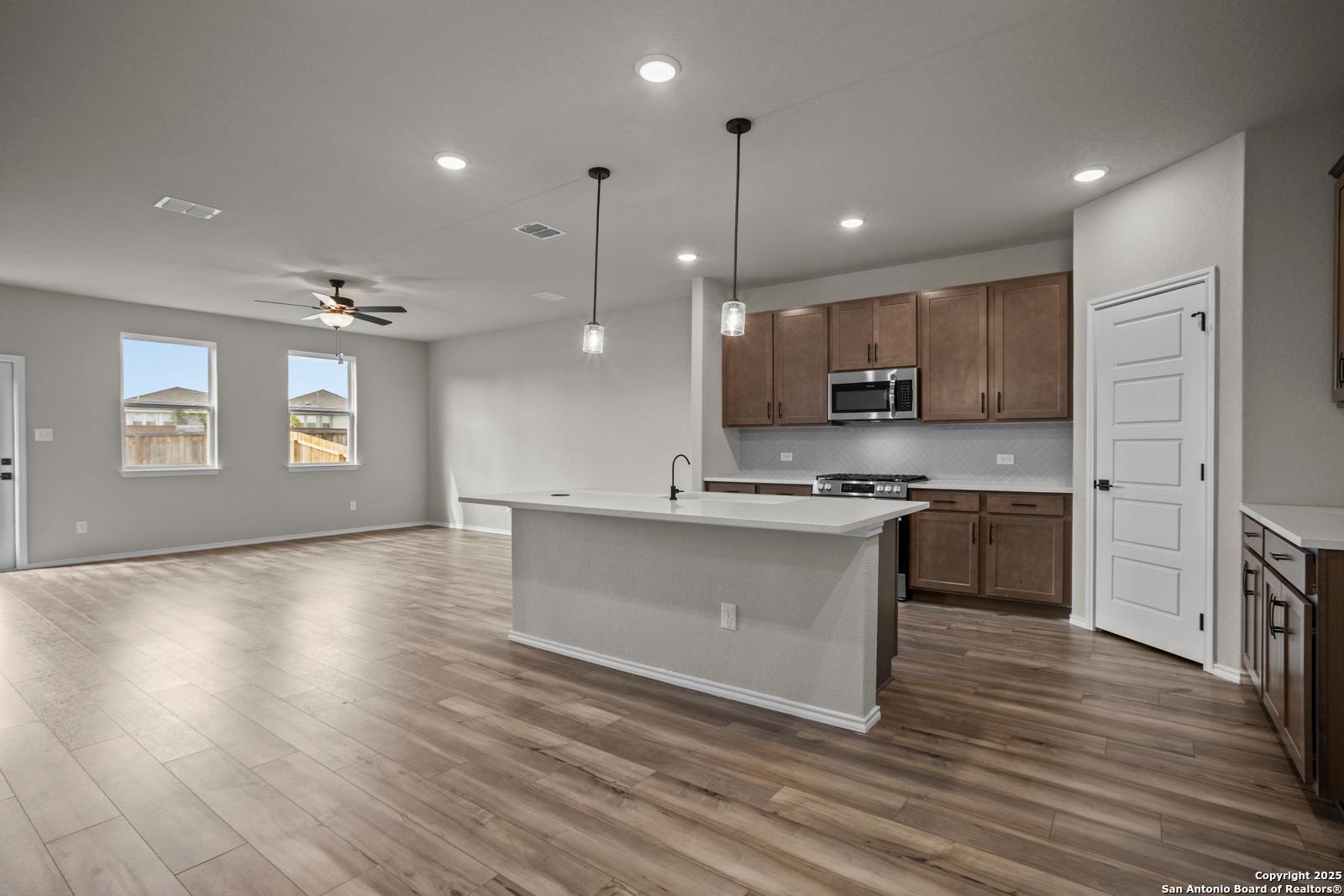 Spacious open kitchen with large white island, brown cabinets, stainless appliances, and hardwood floors in Davidson Homes The Douglas F, San Antonio