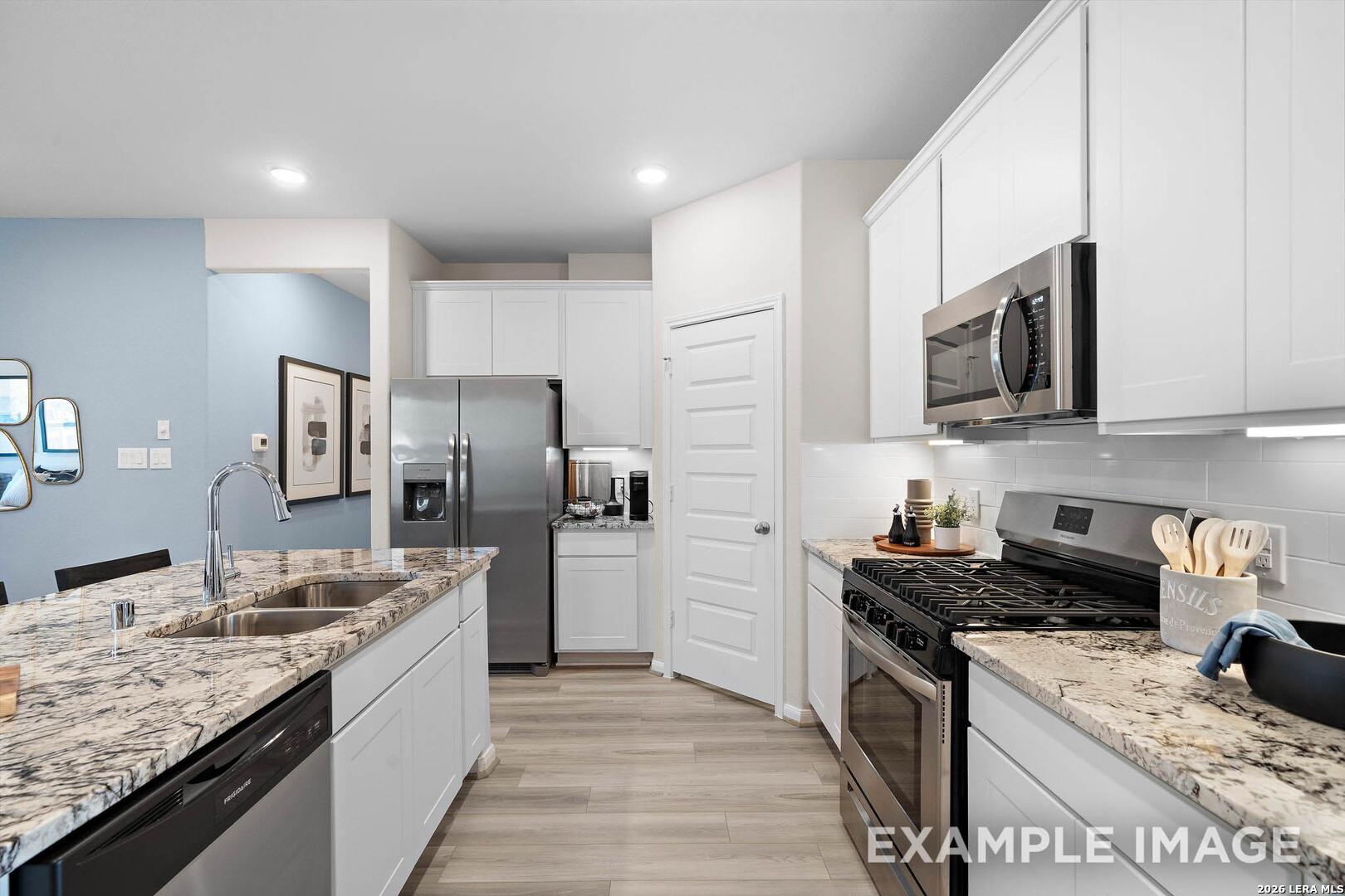 Modern kitchen with granite countertops, stainless steel appliances, and white cabinets in The San Marcos F, San Antonio.