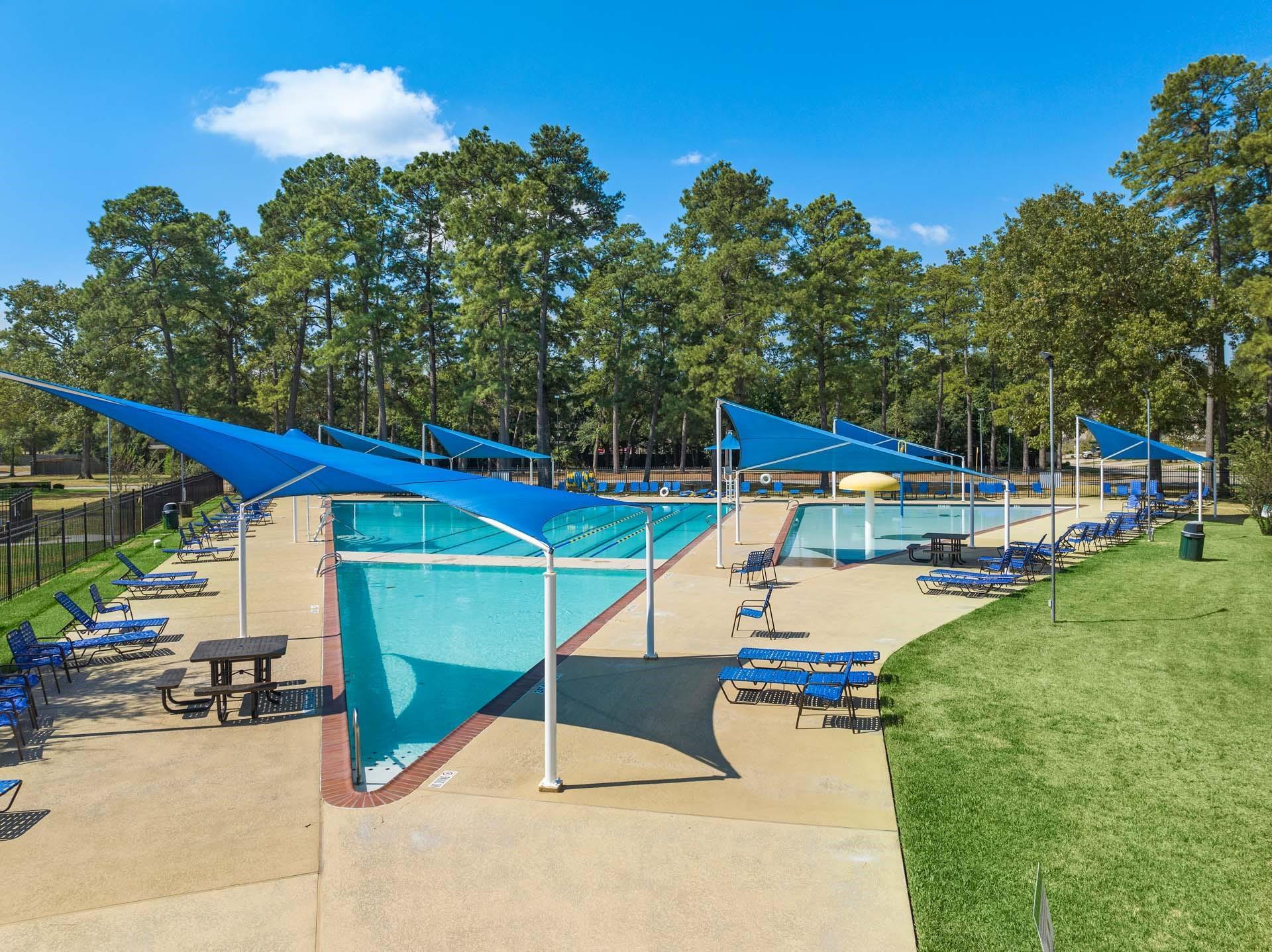 Community swimming pool with blue shade sails and lounge chairs at Enclave at Newport in Crosby, Texas.