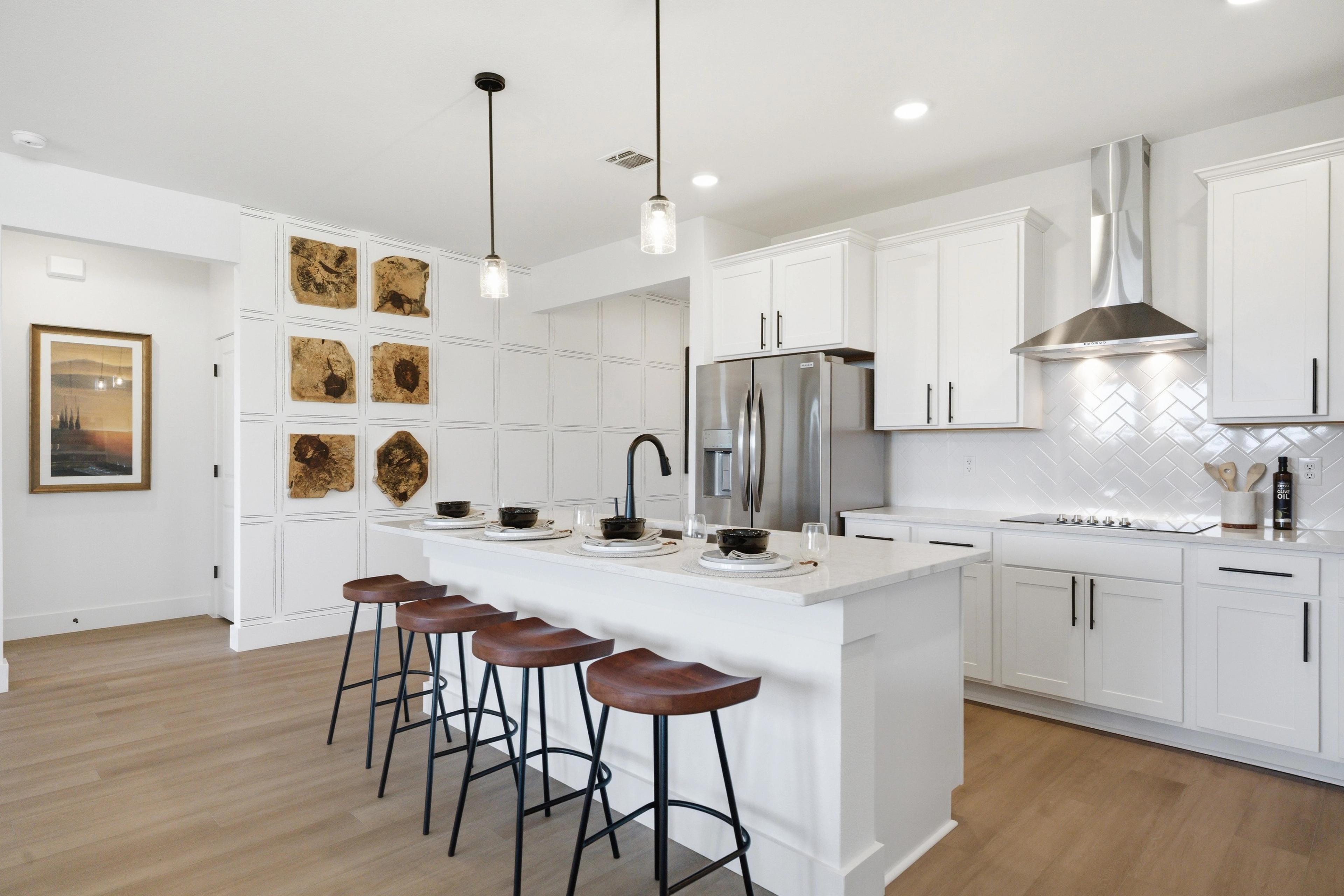 Modern white kitchen with large island, bar stools, stainless appliances, and hardwood floors at Mercer Meadows in Royse City, Texas by Davidson Homes