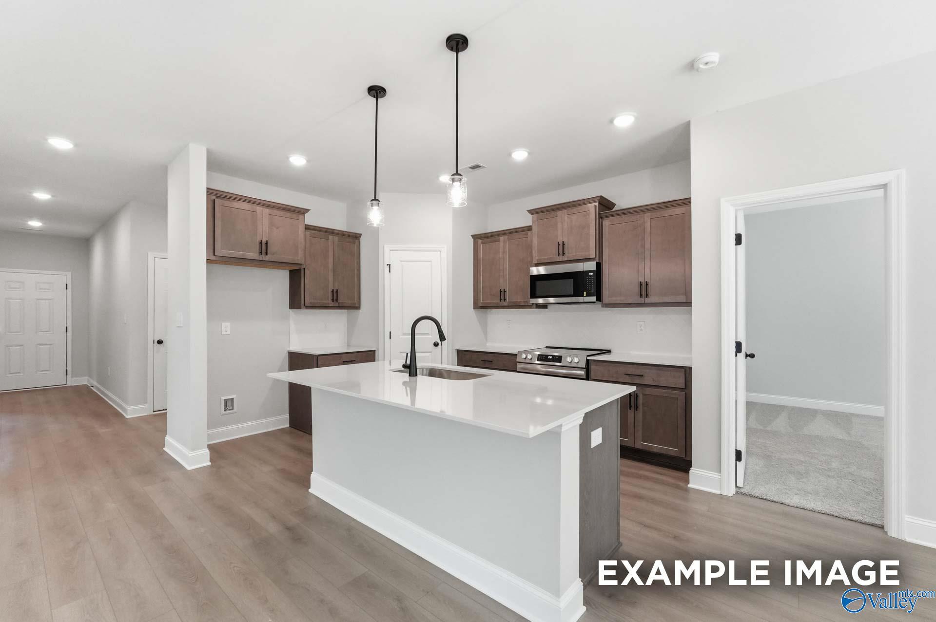Modern kitchen with quartz island, wood cabinets, and stainless appliances in The Franklin C floor plan, Arab, Alabama.