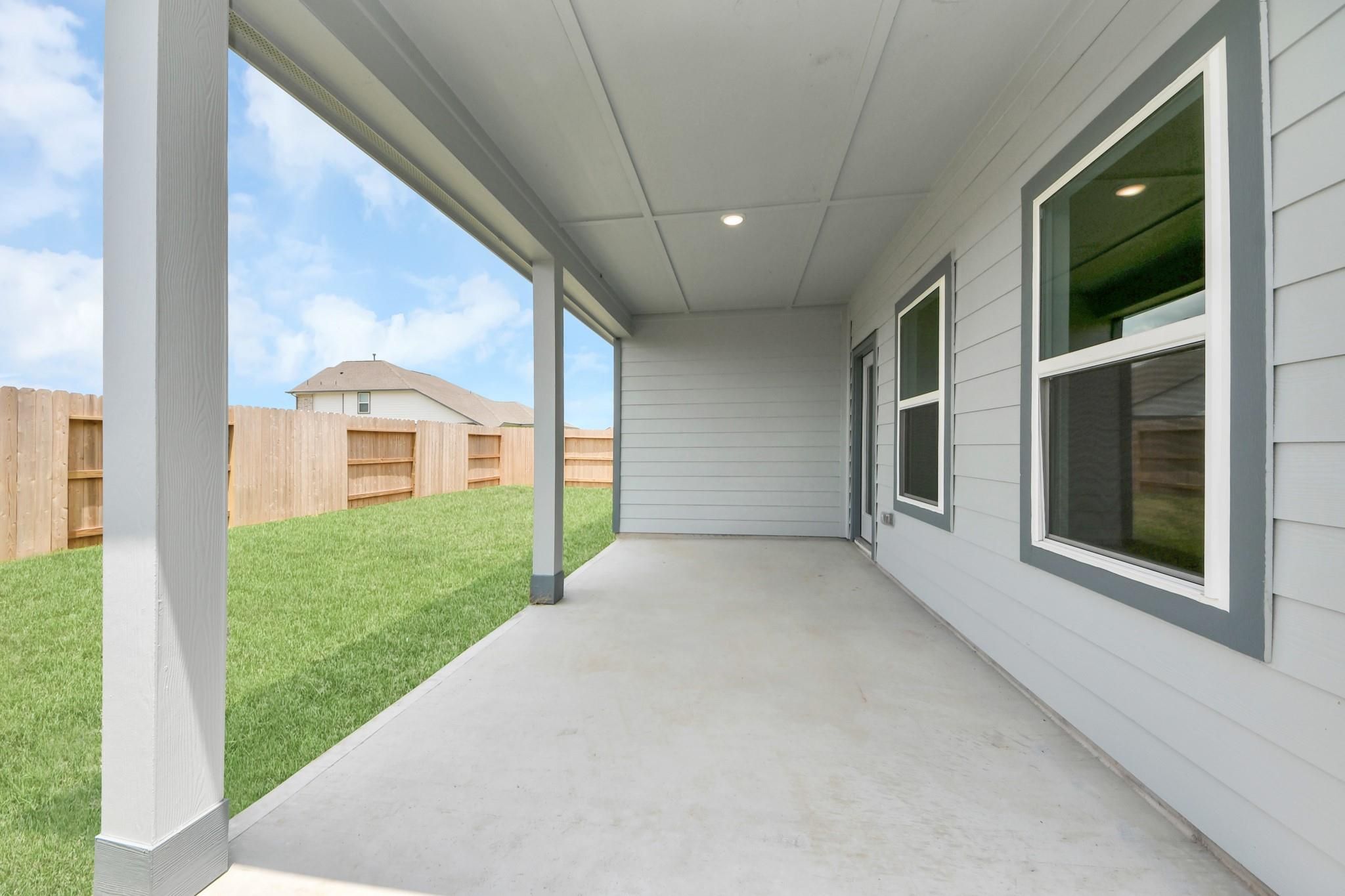 Covered back patio with concrete flooring overlooking the fenced backyard of a Sorrento E home in Sundance Cove, Crosby, TX.