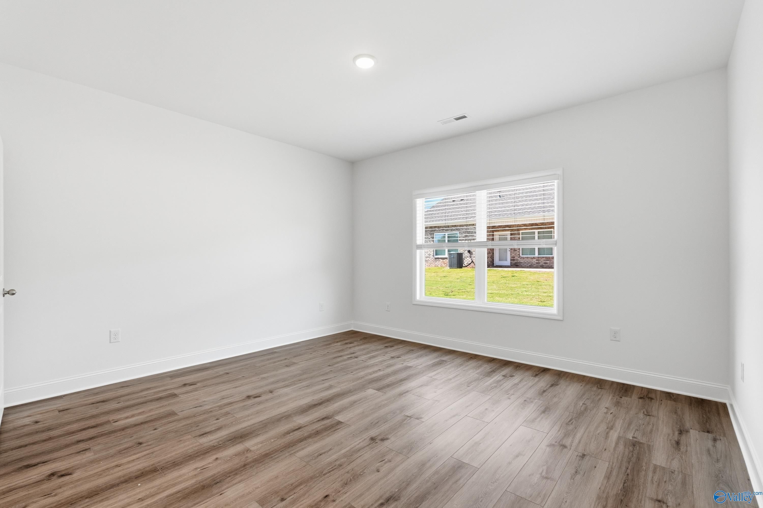 Bright empty bedroom with white walls, hardwood floors, and window view of green lawn in The Cumberland D, Decatur, AL