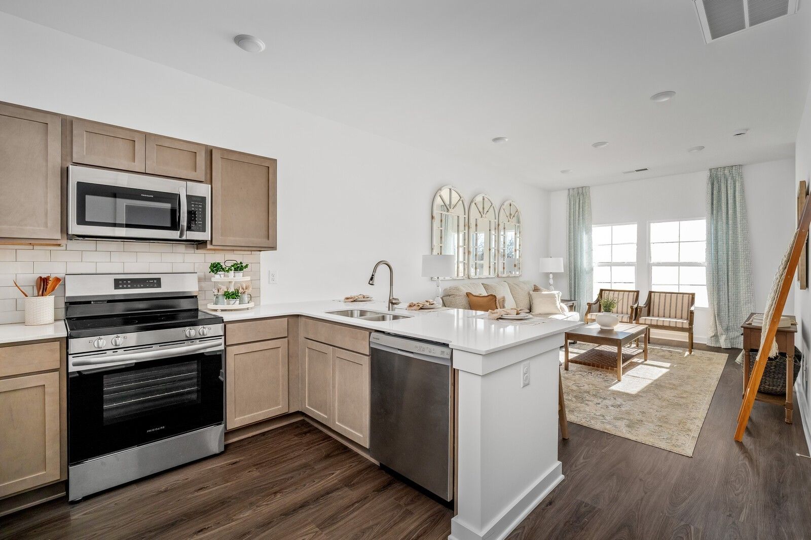 Open-concept kitchen with stainless appliances, beige shaker cabinets, and adjacent living room in Davidson Homes The Cumberland A, Gallatin, TN