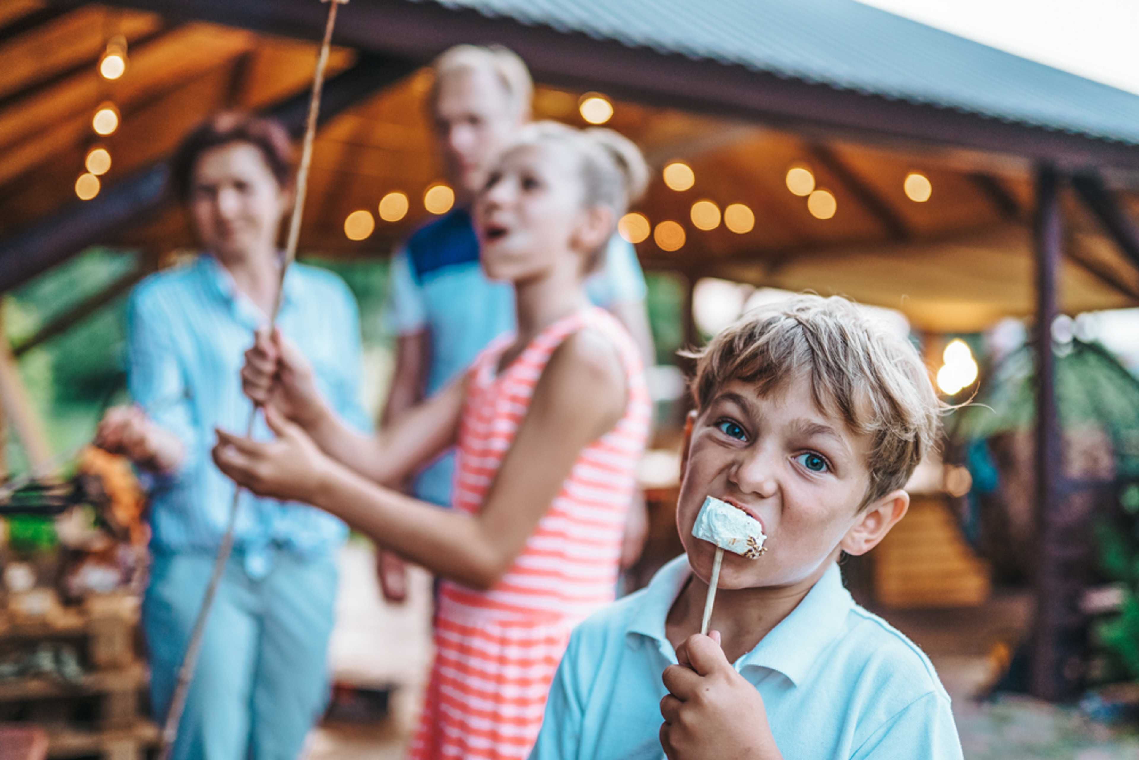 Family roasting marshmallows at Emberly community pavilion in Beasley Texas with string lights and fire pit by Davidson Homes