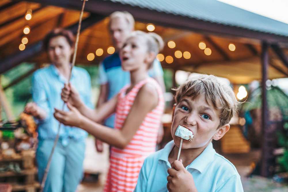 Family roasting marshmallows at Emberly community pavilion in Beasley Texas with string lights and fire pit by Davidson Homes