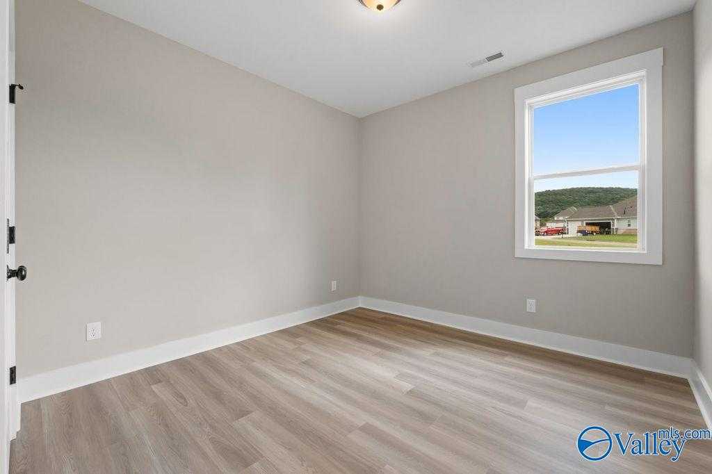 Bright empty secondary bedroom with gray walls, hardwood floors, and large window overlooking neighborhood in Evermore Homes The Oxford, Owens Cross Roads, Alabama