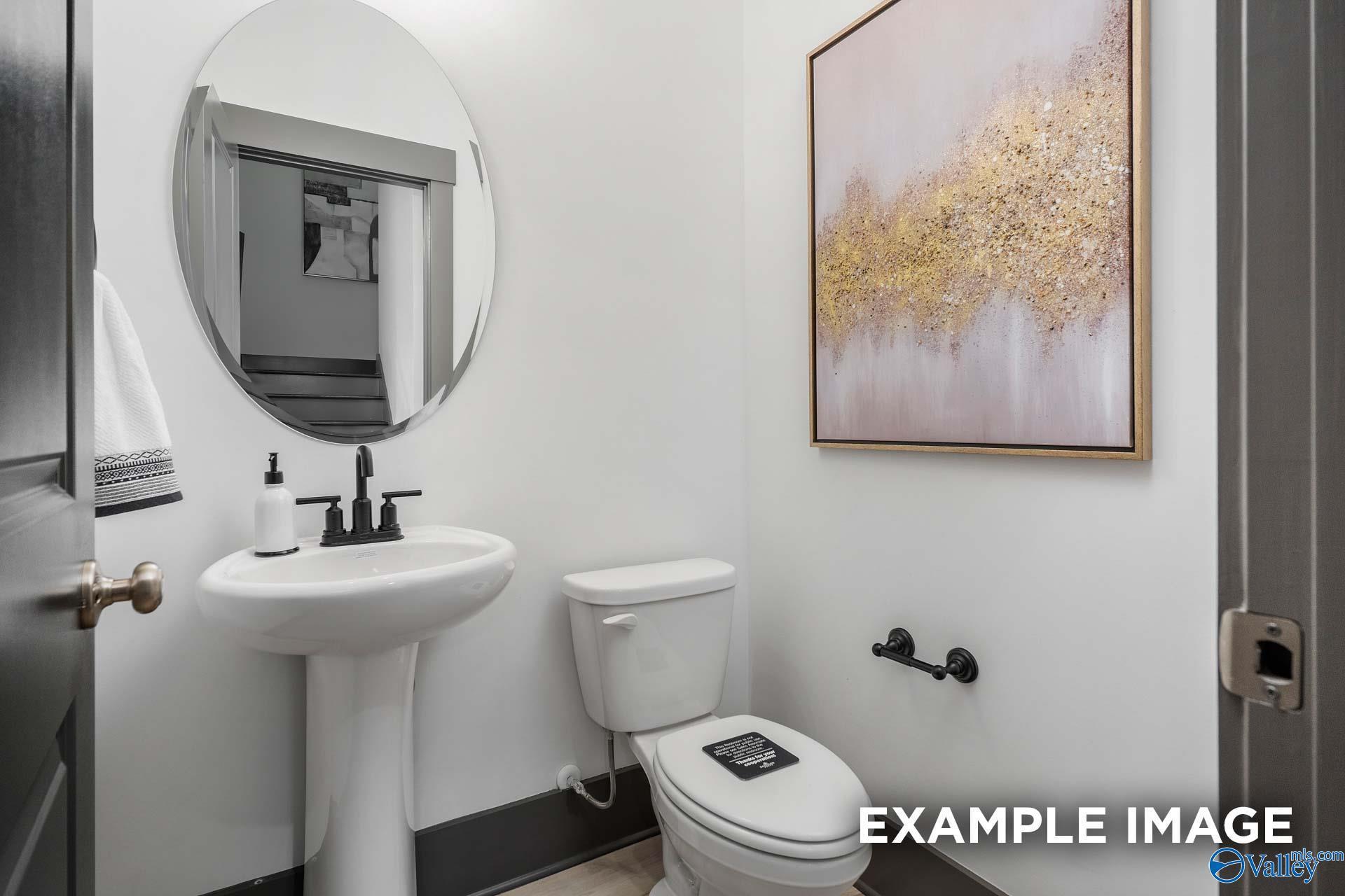 Elegant powder room featuring pedestal sink, round mirror, abstract gold art in Davidson Homes The Rockford B, Madison, Alabama