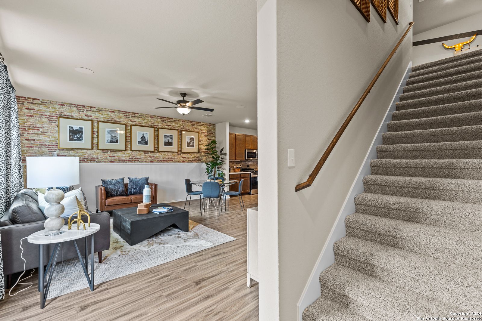 Cozy living room with gray sectional sofa, ceiling fan, and open wooden staircase in Davidson Homes The Douglas F, Bricewood, San Antonio