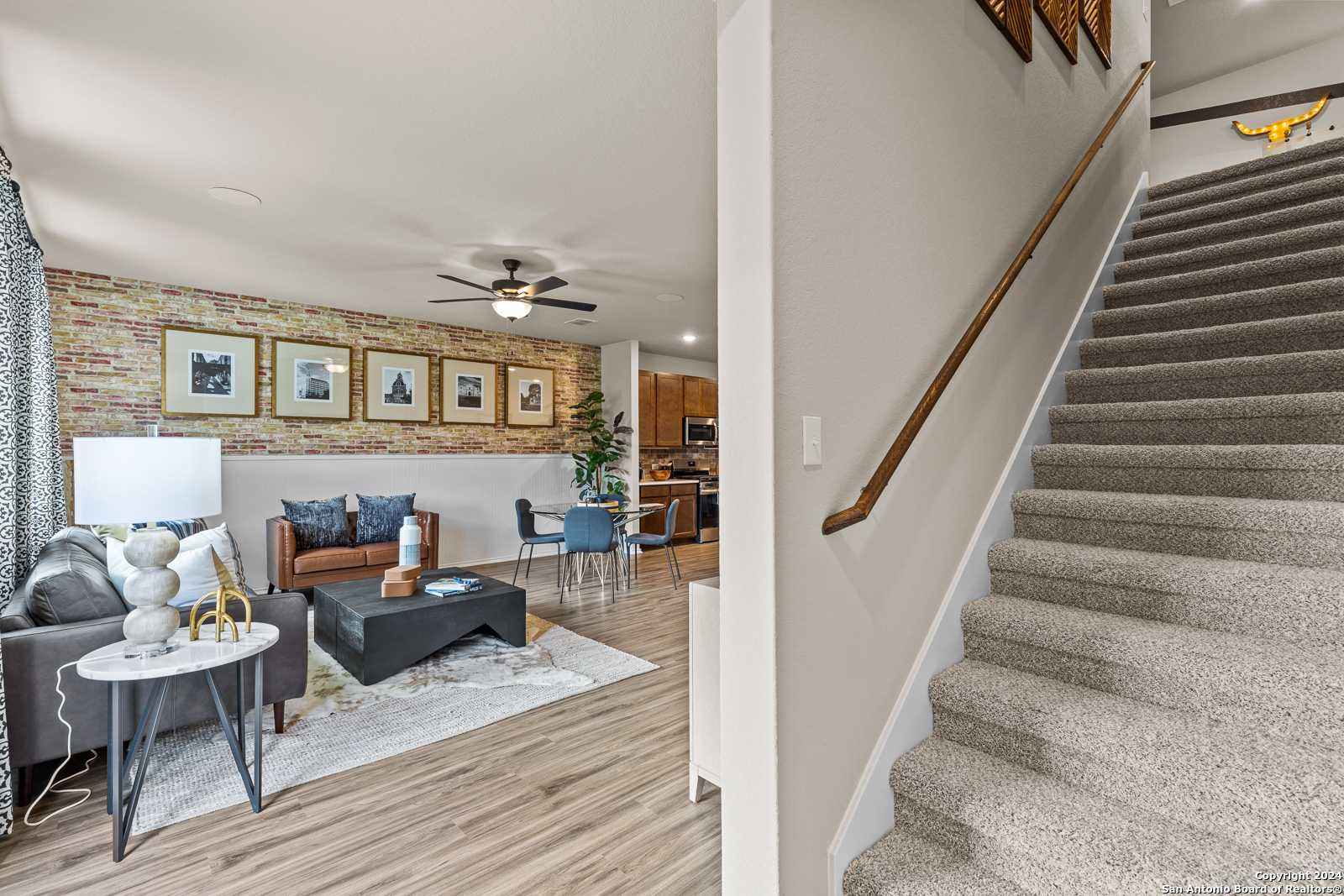 Cozy living room with gray sectional sofa, ceiling fan, and open wooden staircase in Davidson Homes The Douglas F, Bricewood, San Antonio