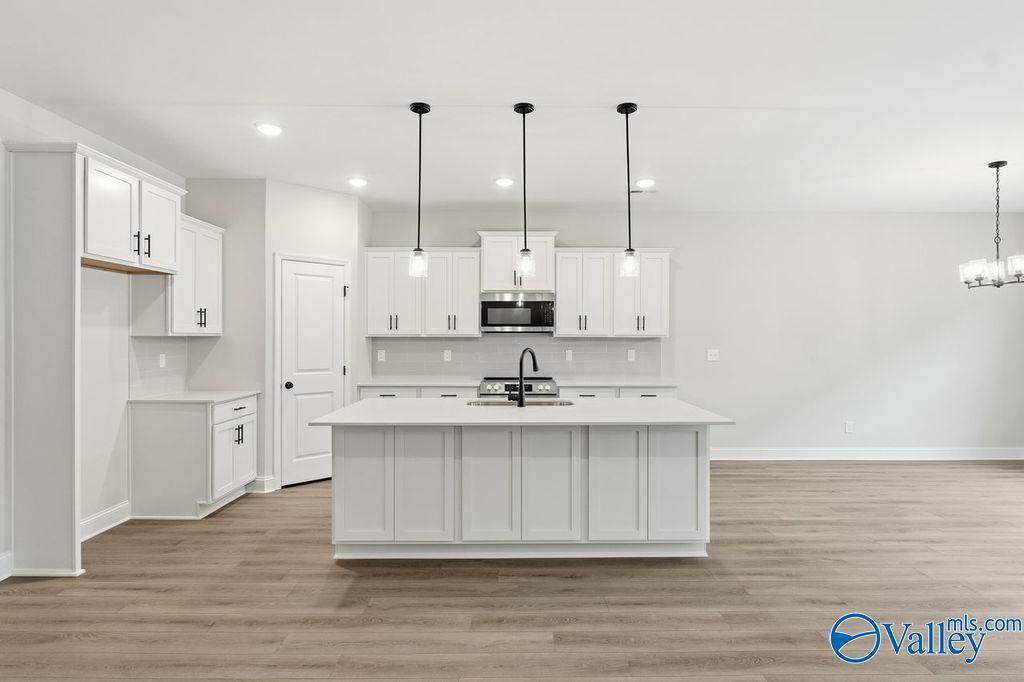 Modern white kitchen with oversized island, stainless steel appliances, and pendant lights in Davidson Homes The Rockford B, Hartselle, Alabama