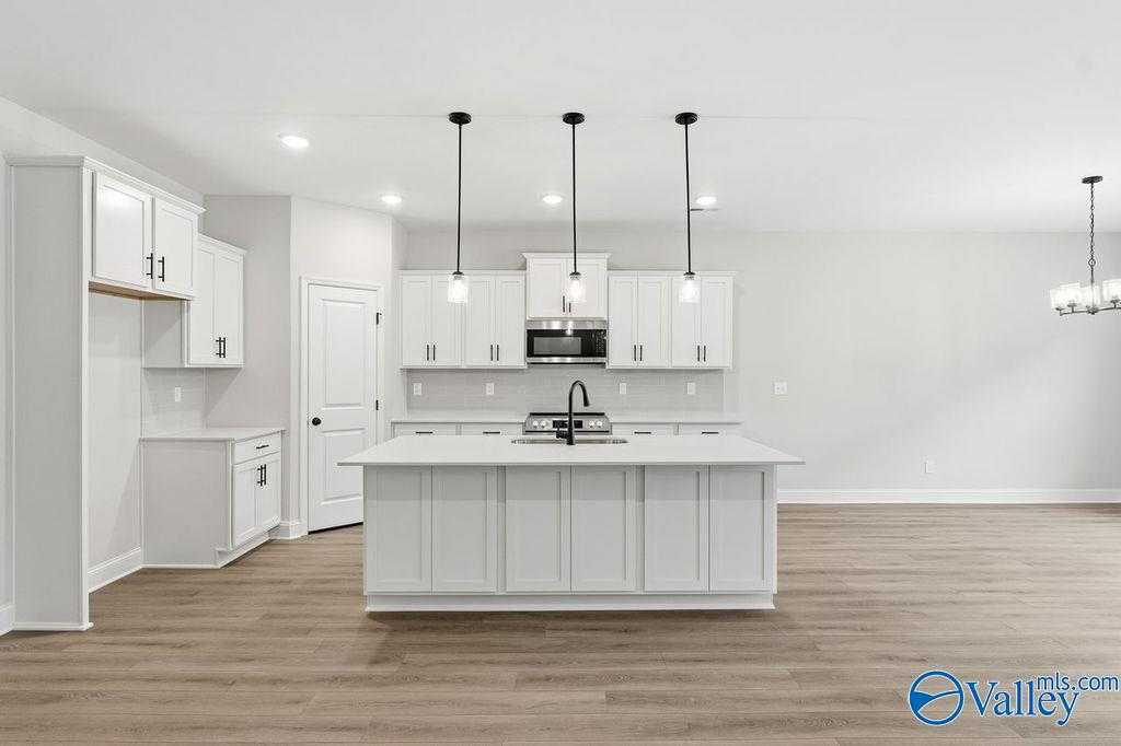 Modern white kitchen with oversized island, stainless appliances, and pendant lights in Davidson Homes The Rockford B, Hartselle, AL