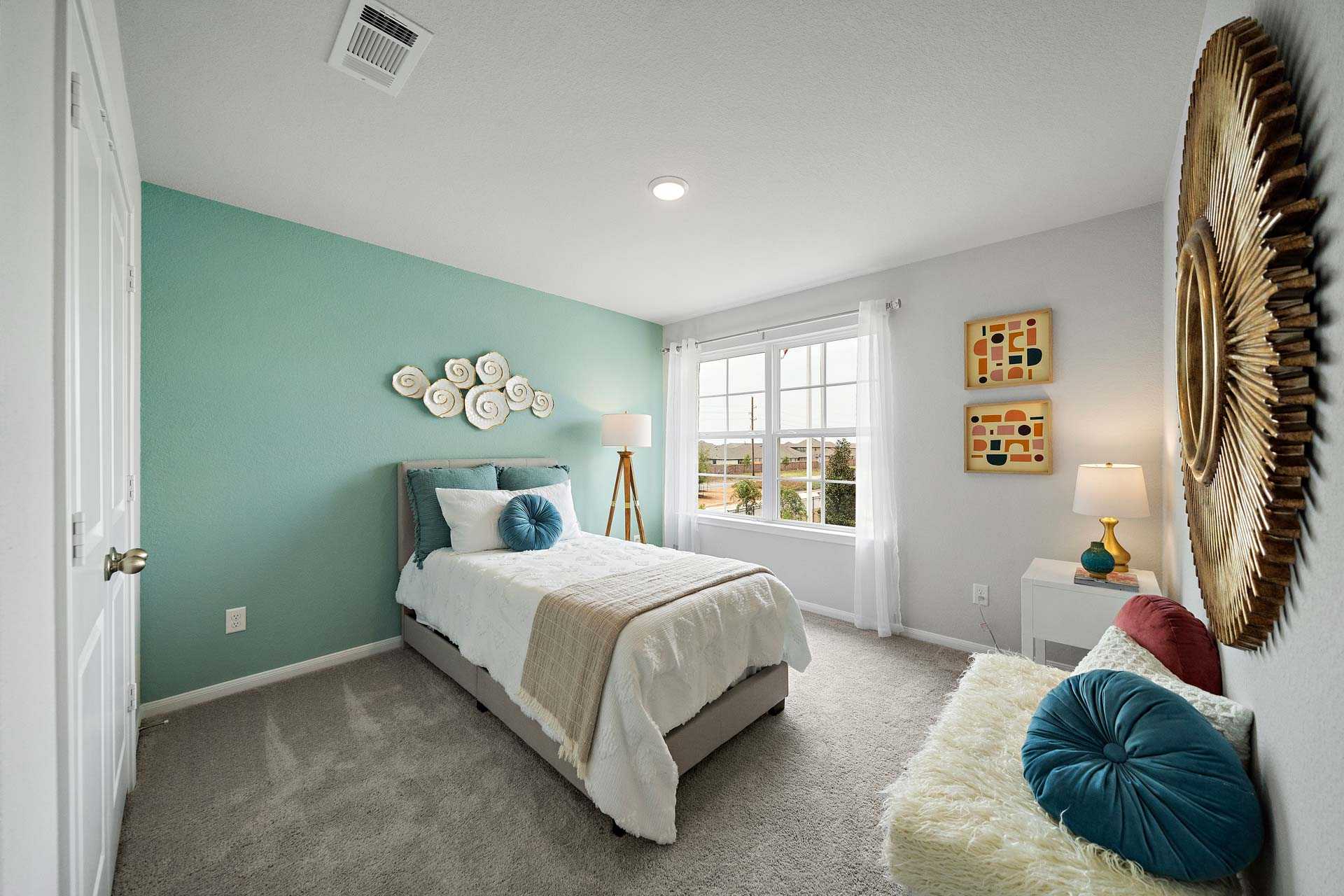 Cozy bedroom at Sunterra in Katy Texas by Davidson Homes with blue accent wall, queen bed, gold mirror, and plush seating