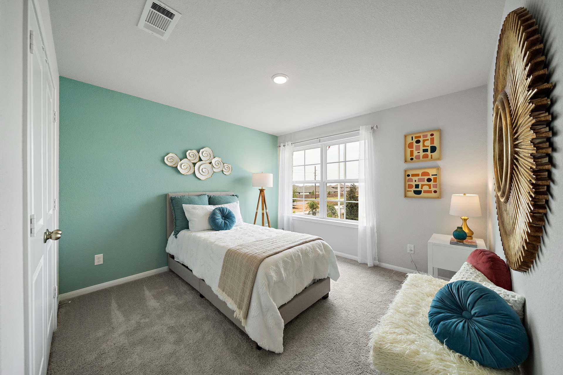 Cozy bedroom at Sunterra in Katy Texas by Davidson Homes with blue accent wall, queen bed, gold mirror, and plush seating