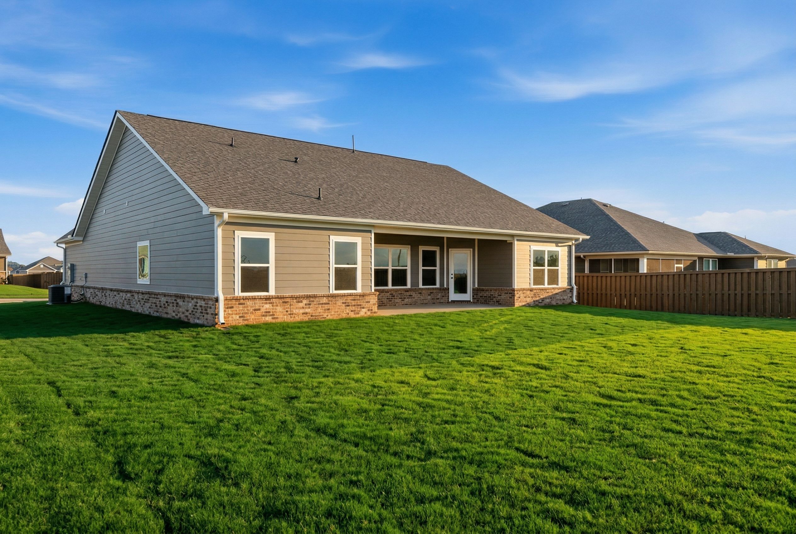 Rear view of The Rockford single-story home with covered porch, stone and siding exterior, lush green lawn, Cullman AL