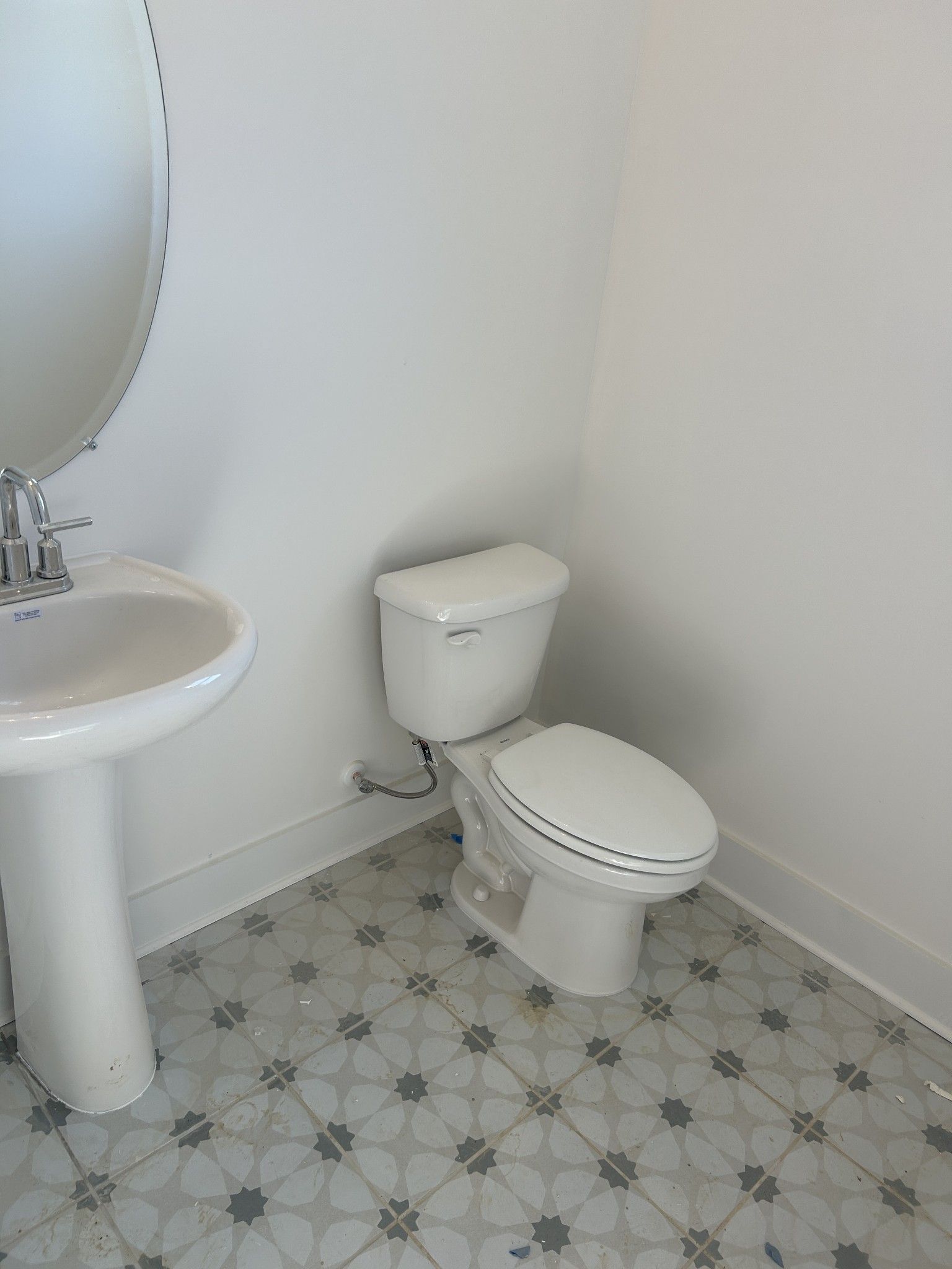 Clean white powder room with pedestal sink, oval mirror, white toilet, and star-patterned tile floor in Davidson Homes The Henry C, Mt. Juliet