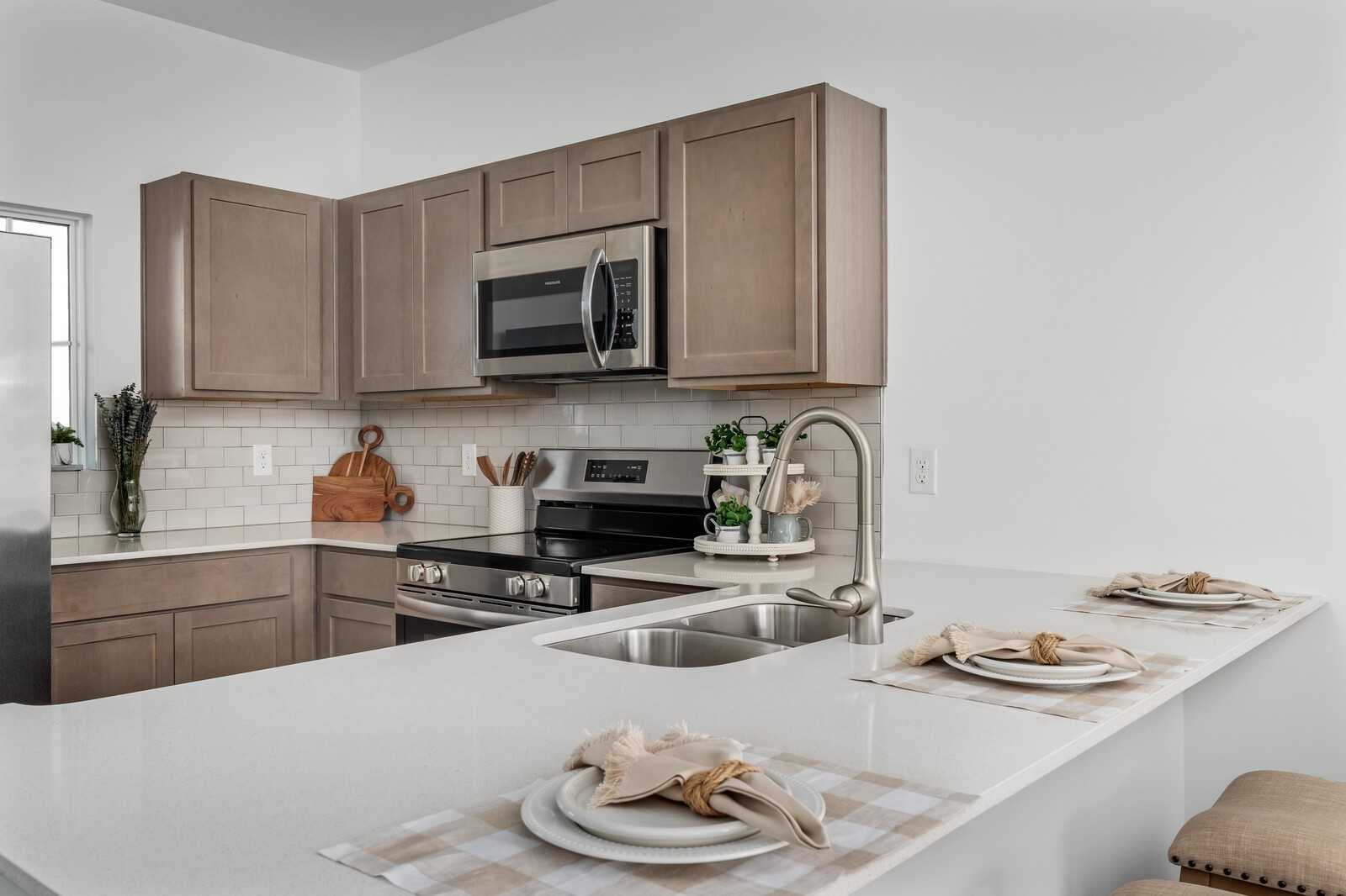 Modern kitchen featuring taupe shaker cabinets, stainless steel appliances, subway tile backsplash, and quartz island in Davidson Homes Cumberland A, Gallatin, TN