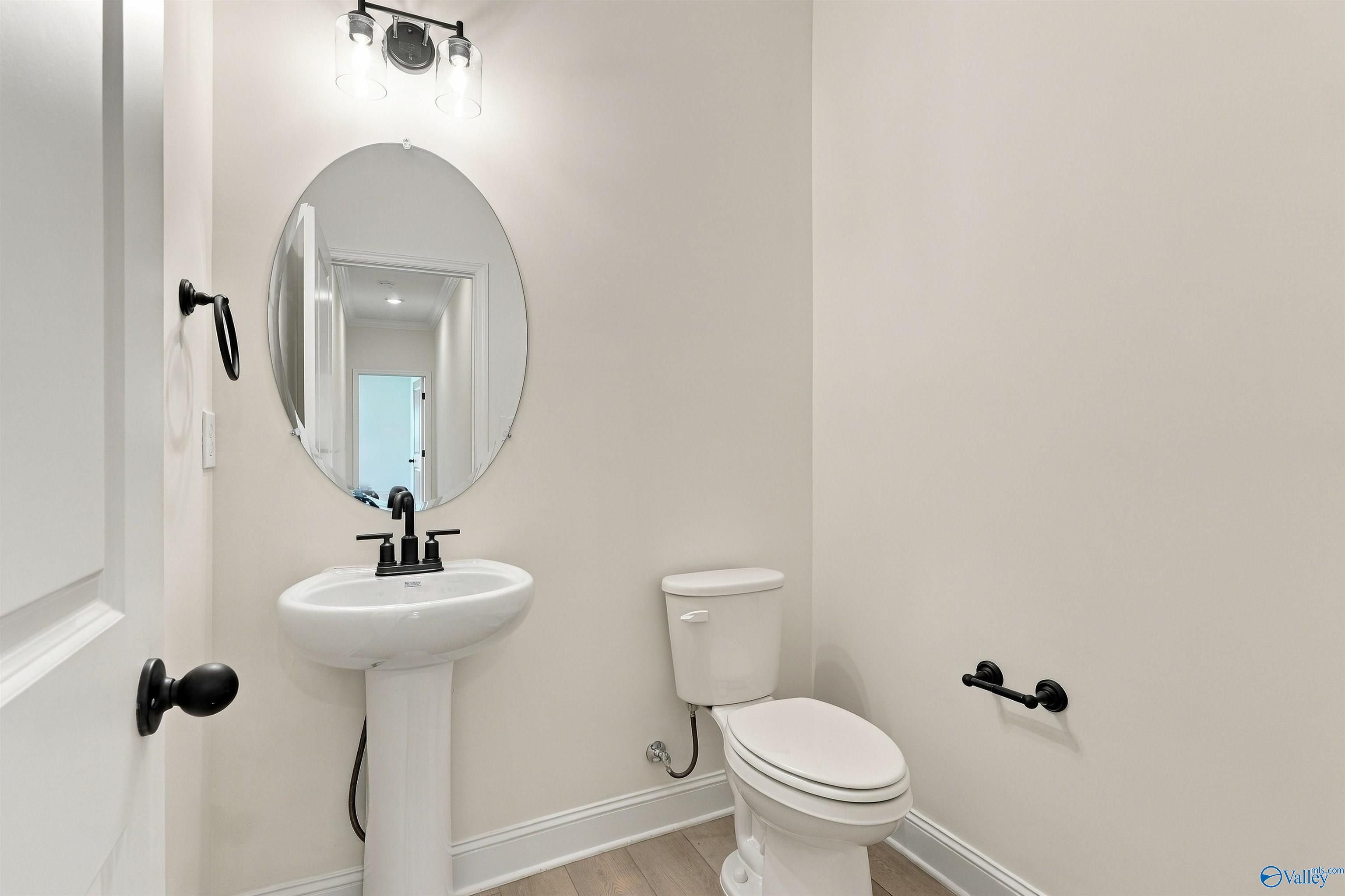 Elegant powder room with pedestal sink, black fixtures, and round frameless mirror in Davidson Homes The Valencia, Huntsville, Alabama