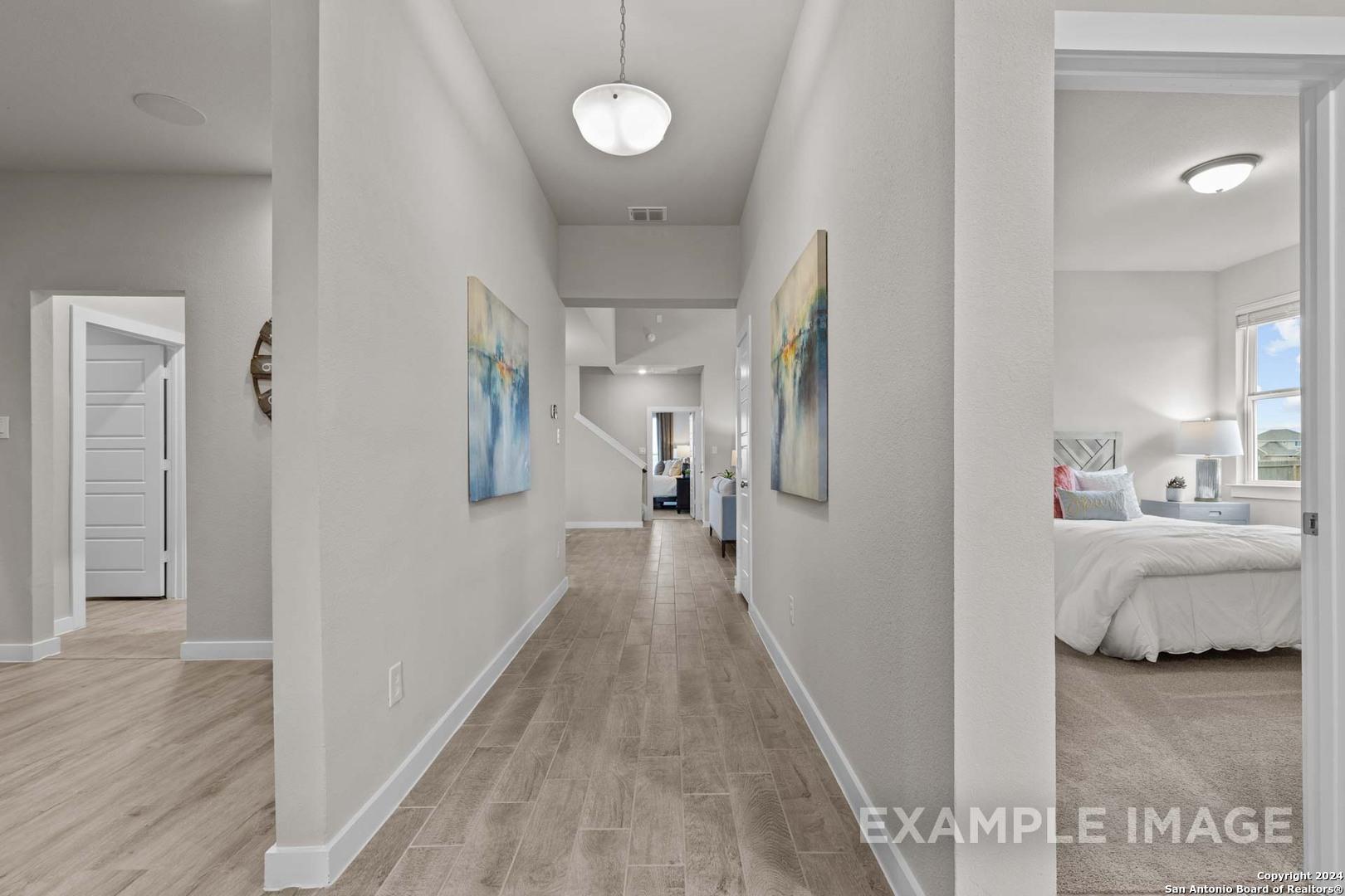 Elegant hallway with abstract blue paintings, wood floors, and open bedroom door in Davidson Homes The Collin A, Seguin, Texas