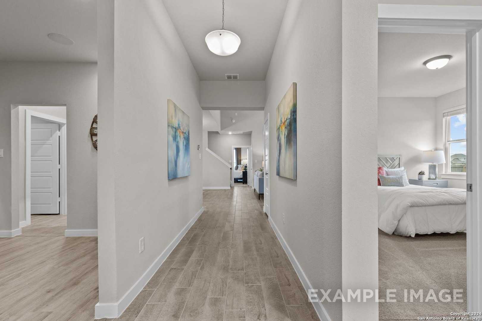 Spacious hallway with abstract artwork and light wood floors leading to serene bedroom in Davidson Homes The Collin B, Seguin, Texas