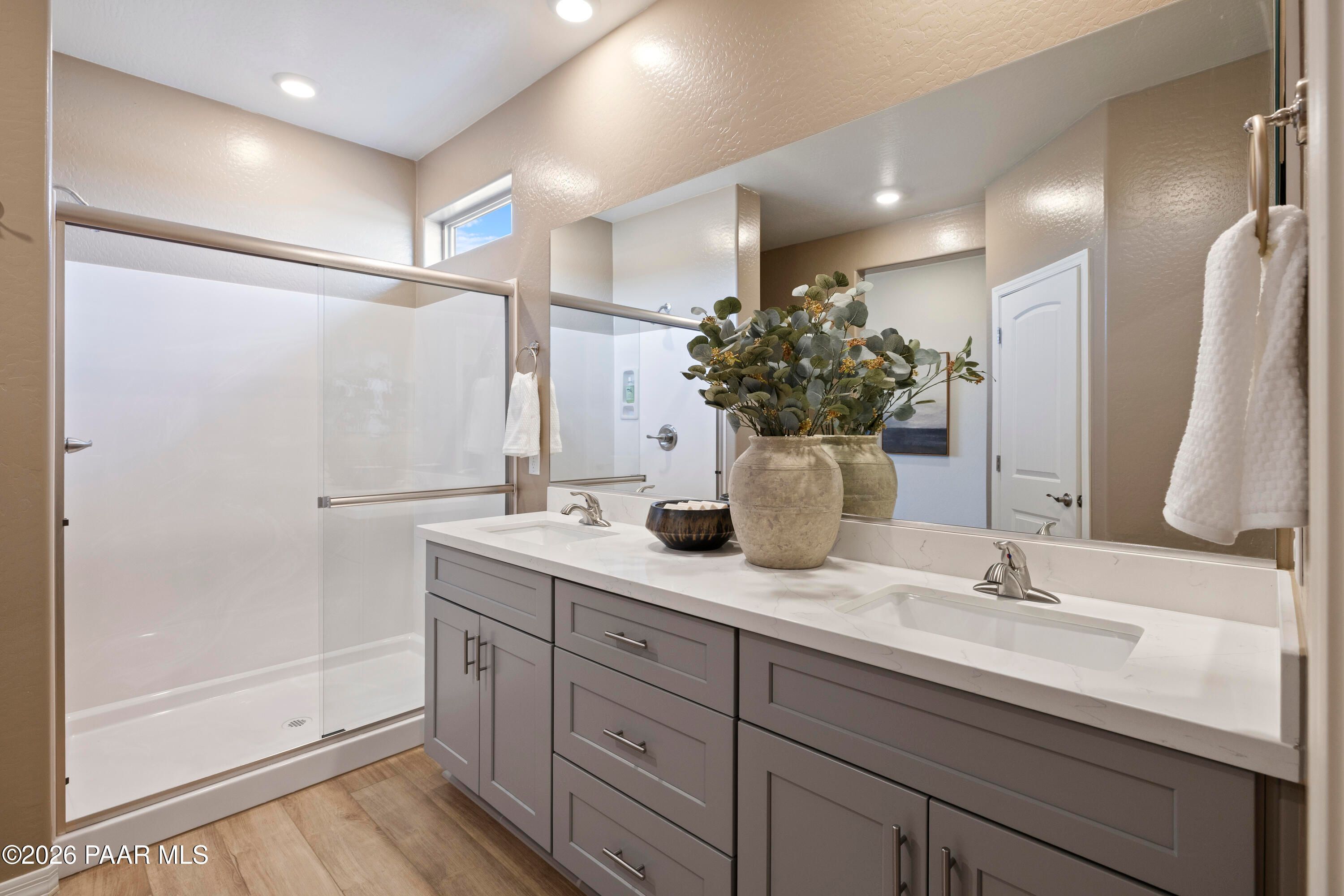 Modern primary bathroom with double vanity, quartz countertops, and glass-enclosed shower in The Harmony A, Pronghorn Ranch.
