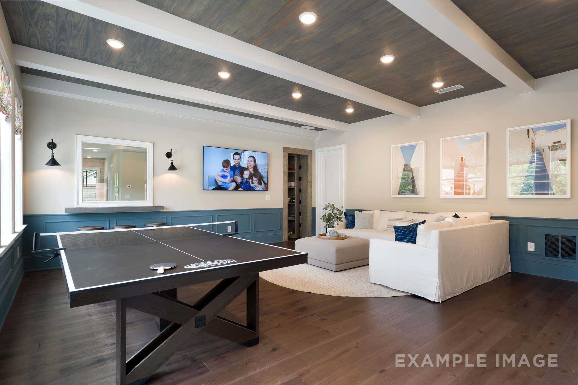 Spacious game room in The Seaside home featuring table tennis table, wall-mounted TV, white sectional sofa, and beamed ceiling with hardwood floors