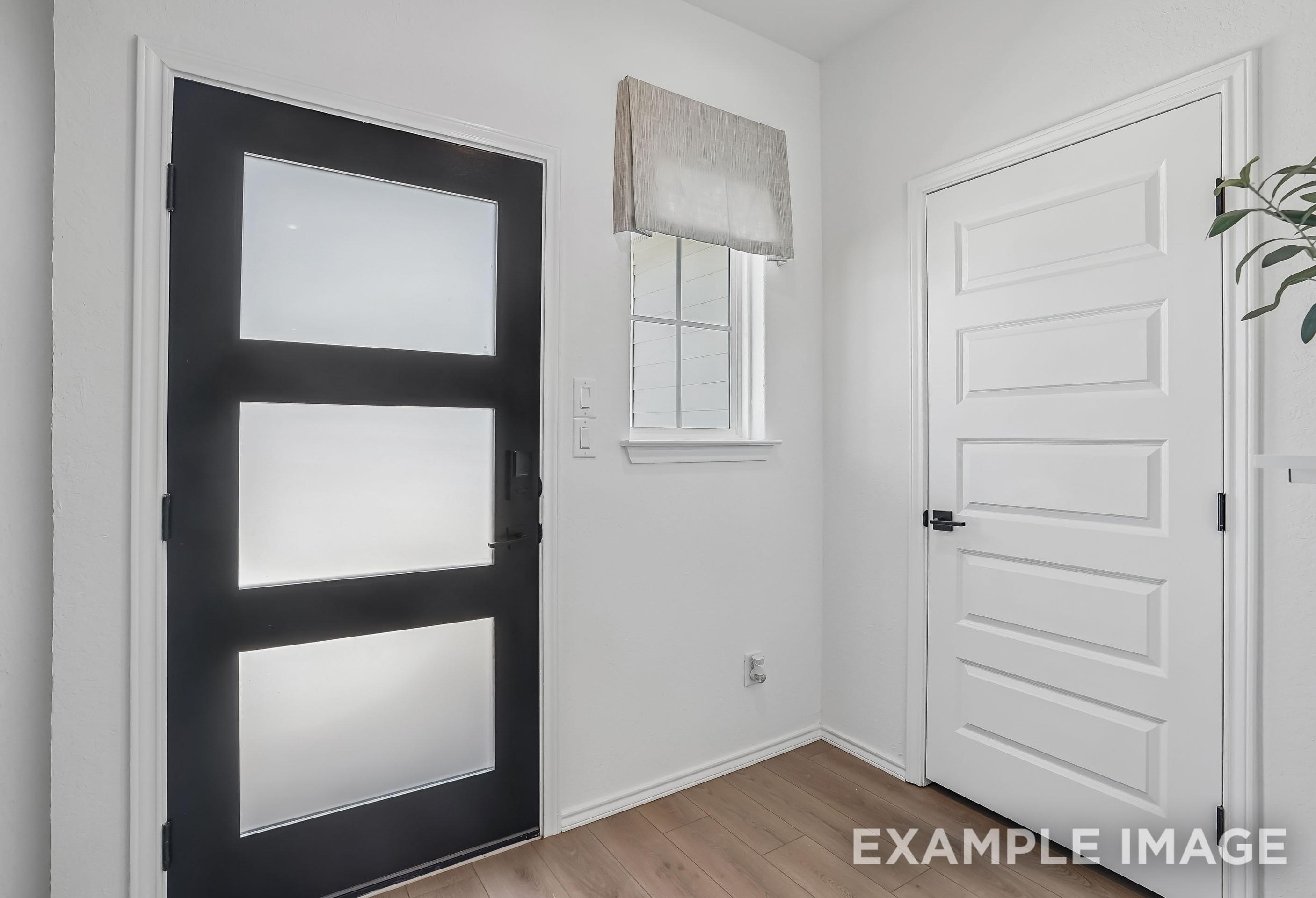Modern entryway of The Pinecrest B featuring a contemporary black door with frosted glass panels and wood-style flooring.