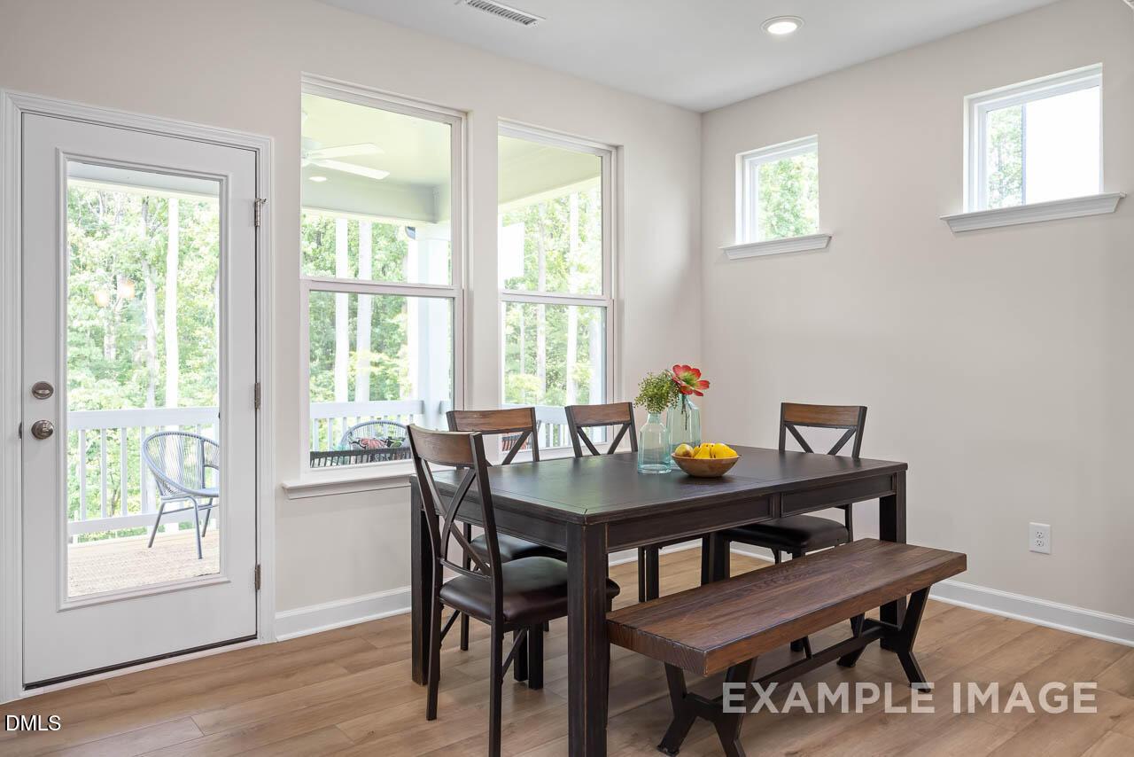 Bright dining room with wooden table, upholstered chairs, bench, flowers, and fruit overlooking wooded deck in Lillington, NC home