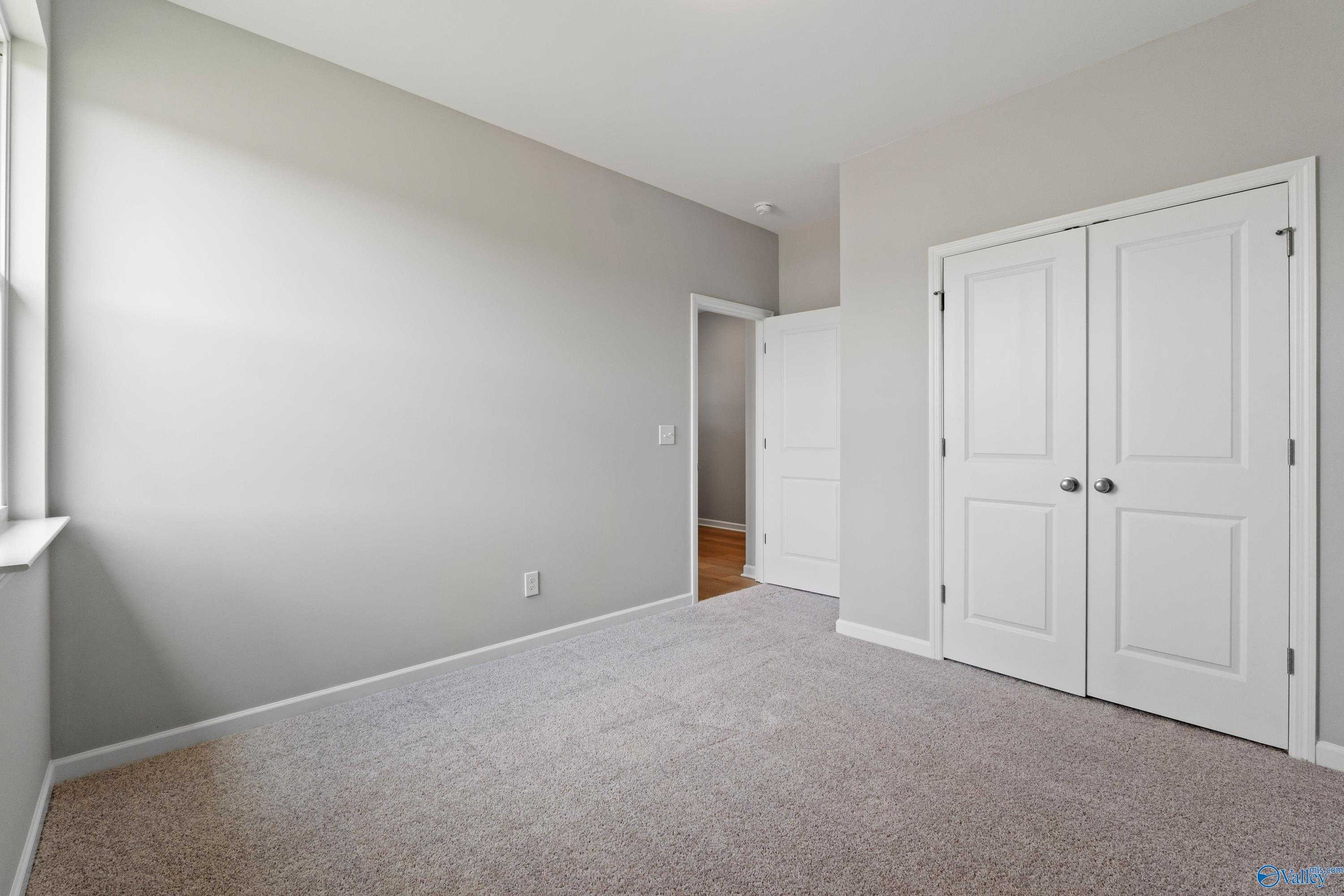 Bright bedroom with light gray walls, plush carpet, double-door closet in Evermore Homes The Aurora, Harvest AL