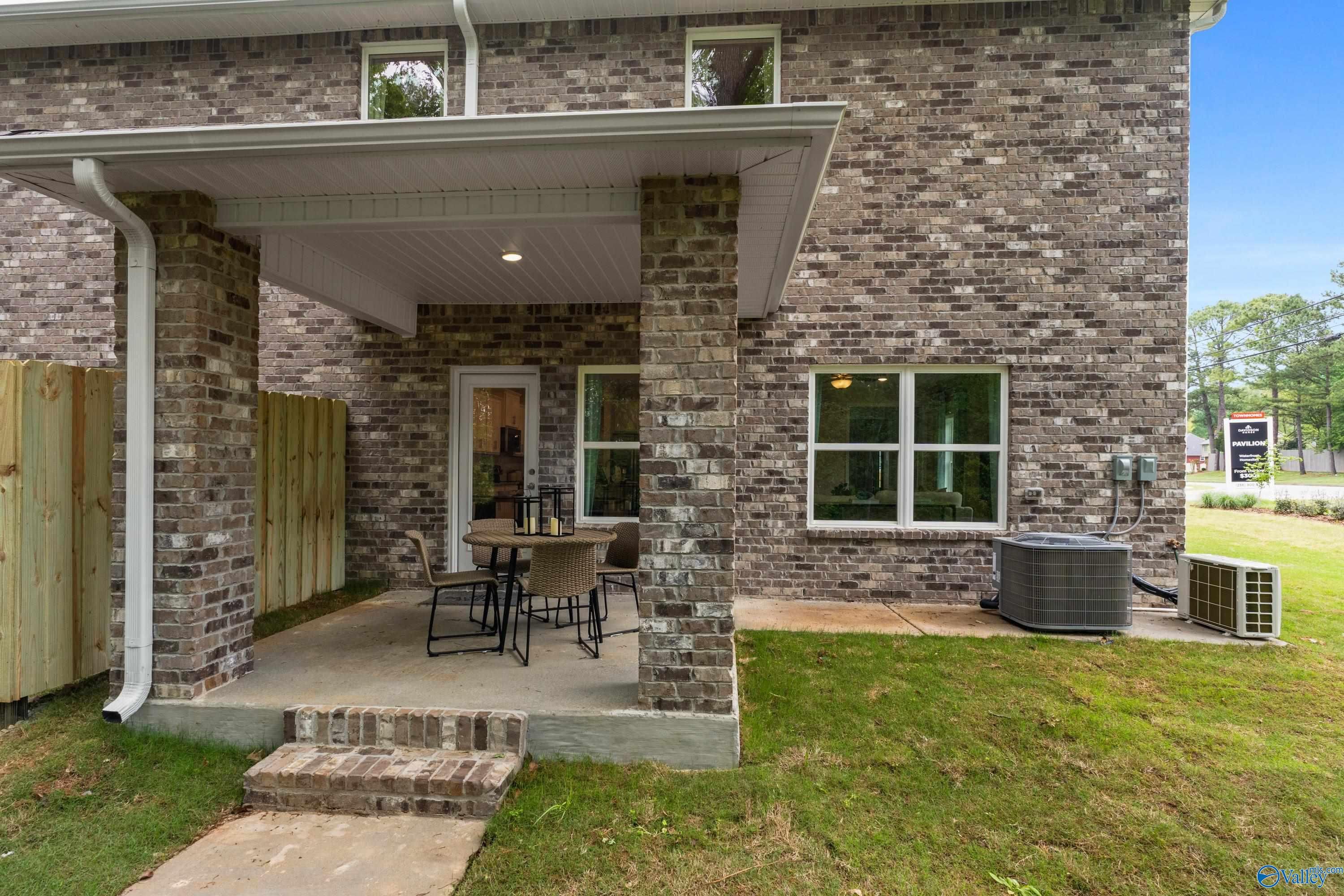 Covered rear patio with brick columns and outdoor seating on green lawn in Davidson Homes The Camden, Pavilion, Huntsville, Alabama