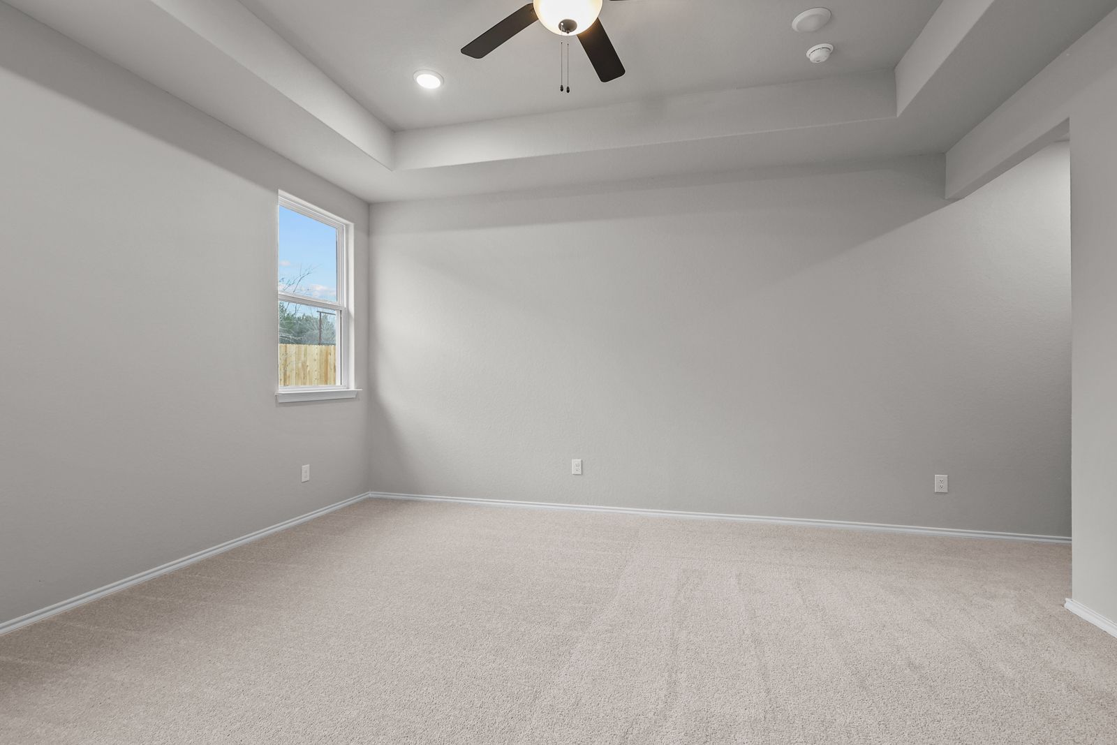 Spacious master bedroom in The Glenwood E featuring a tray ceiling, plush carpeting, and natural light from the window.