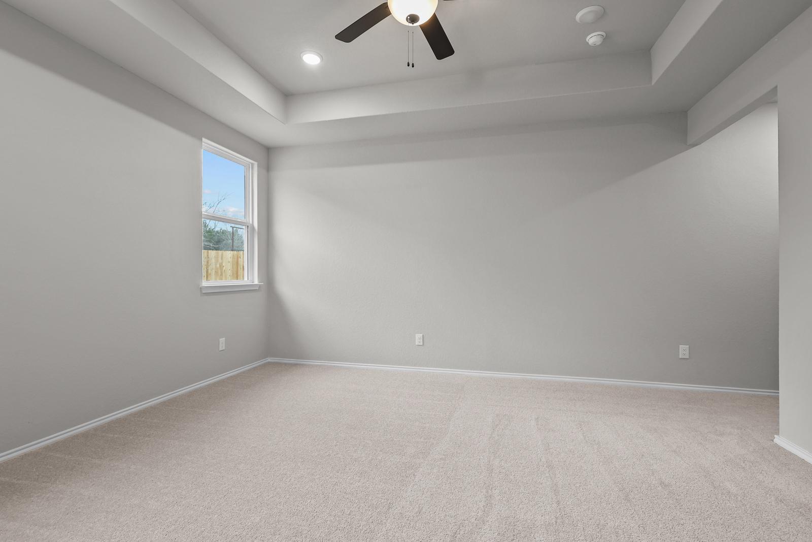 Spacious master bedroom in The Glenwood E featuring a tray ceiling, plush carpeting, and natural light from the window.