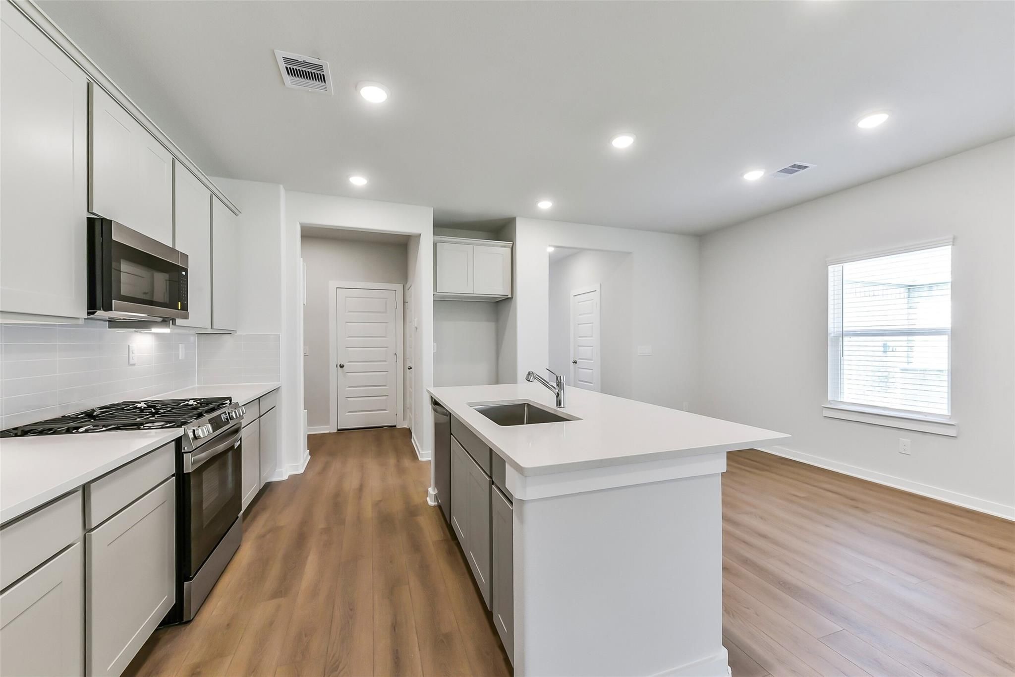 Modern white kitchen with stainless appliances, gas cooktop, and quartz island in Davidson Homes Brazos E, Magnolia TX