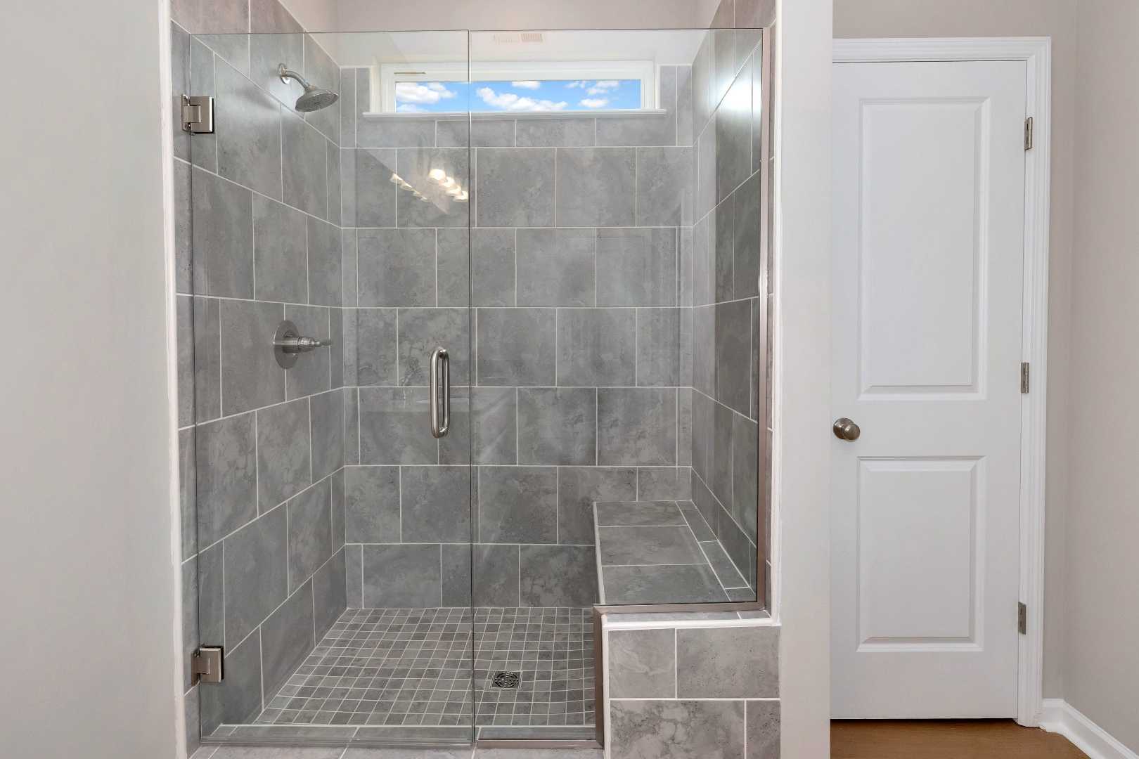 Modern gray tiled walk-in shower with frameless glass enclosure and built-in bench at Links Crossing in Auburn, Alabama