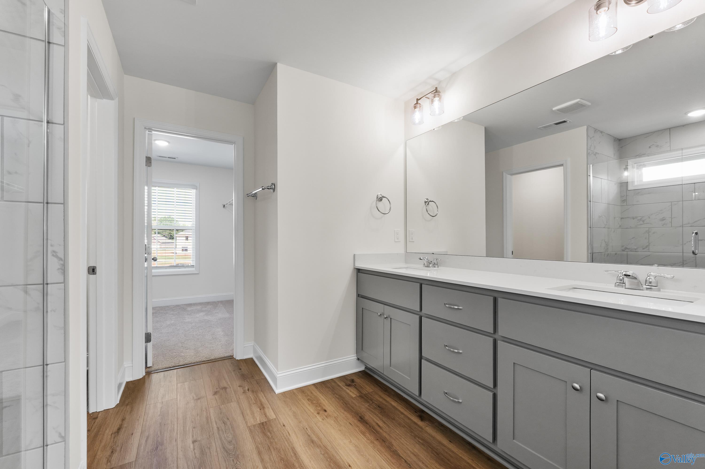 Master bathroom with double vanity, gray cabinets, glass shower, and hardwood floors in Davidson Homes Shelby A, Athens AL