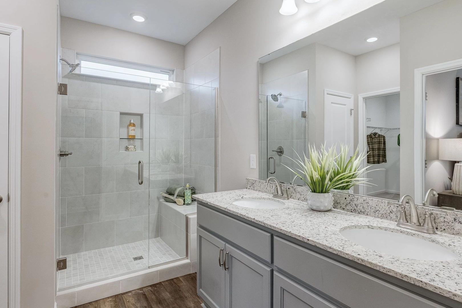 Modern master bathroom at Carroll Green in Harvest Alabama with double gray vanity, frameless glass shower, and hardwood floors